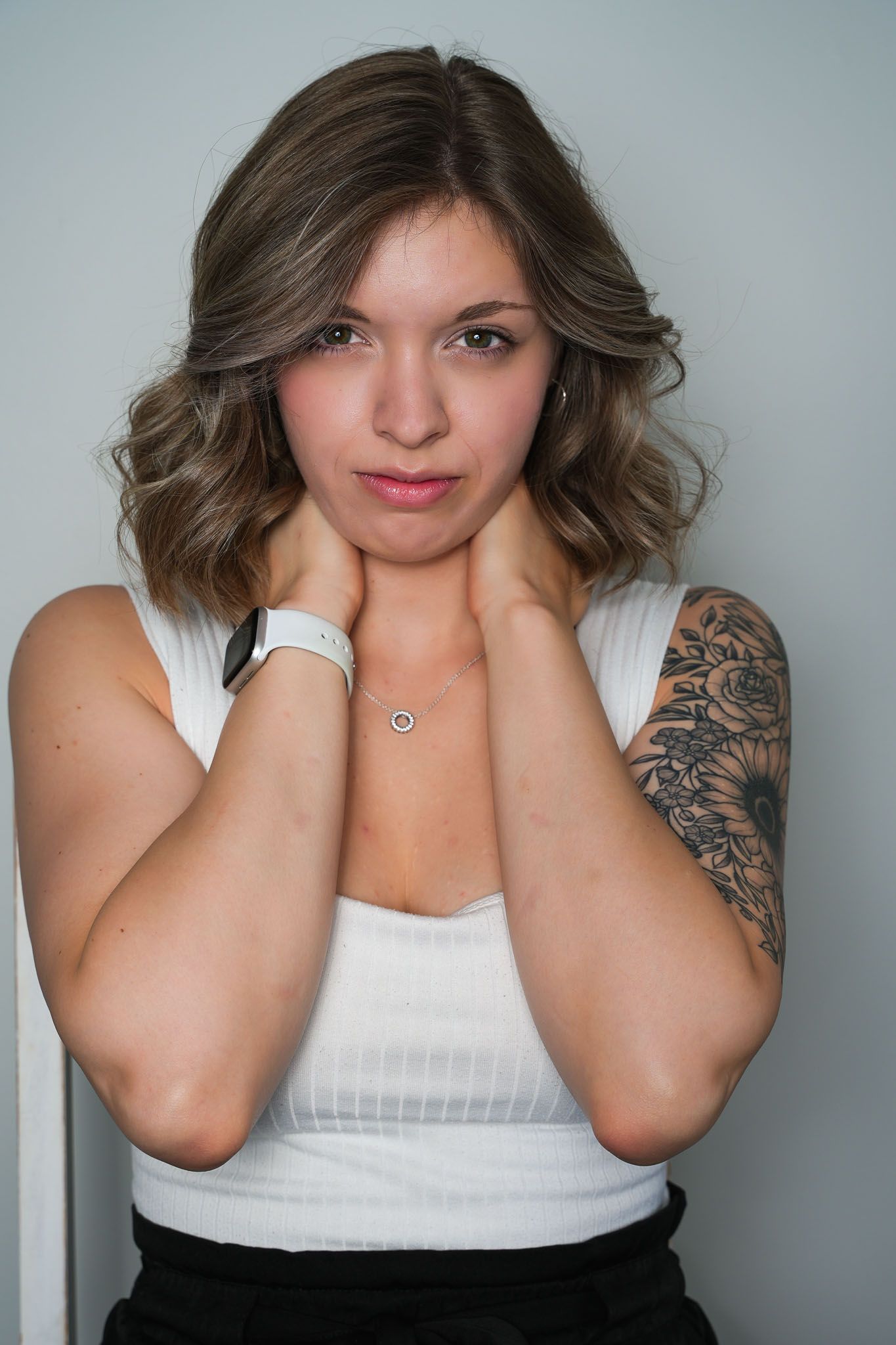 Portrait series featuring someone in a white tank top with visible arm tattoos against a gray wall.