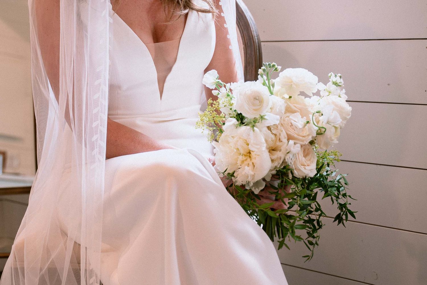 A white wedding dress hangs elegantly against a light background with delicate lace details and flowing fabric.