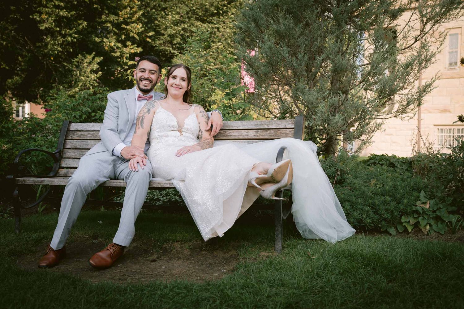 Casual wedding portraits on wooden bench in garden setting.