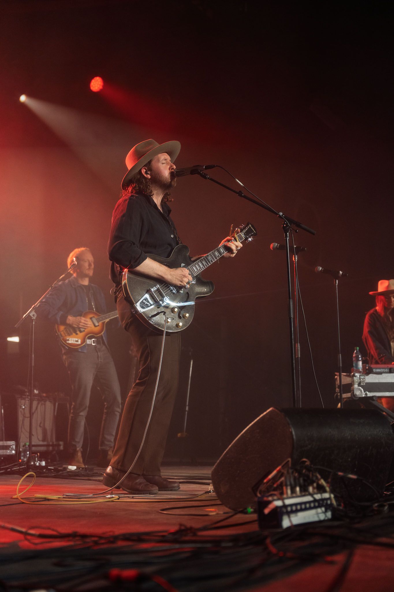 The Paper Kites band members performing on dimly lit stage with red lighting and musical instruments.