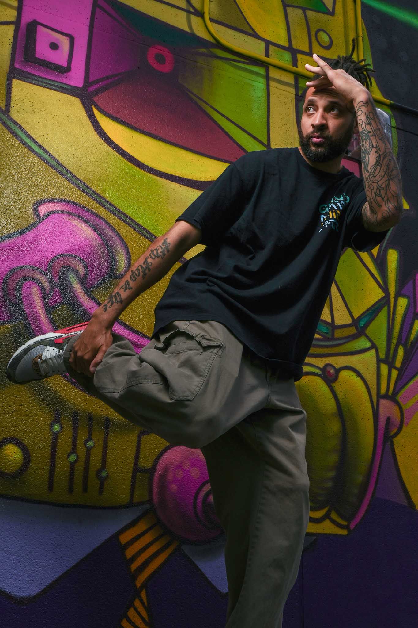 Breakdancer performs dynamic moves against colorful graffiti wall in urban setting.