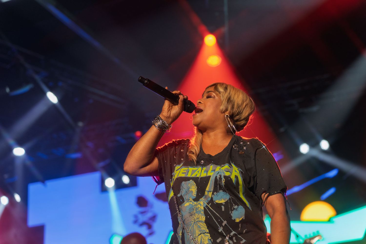 Concert performer in graphic t-shirt singing on stage with colorful lighting effects.