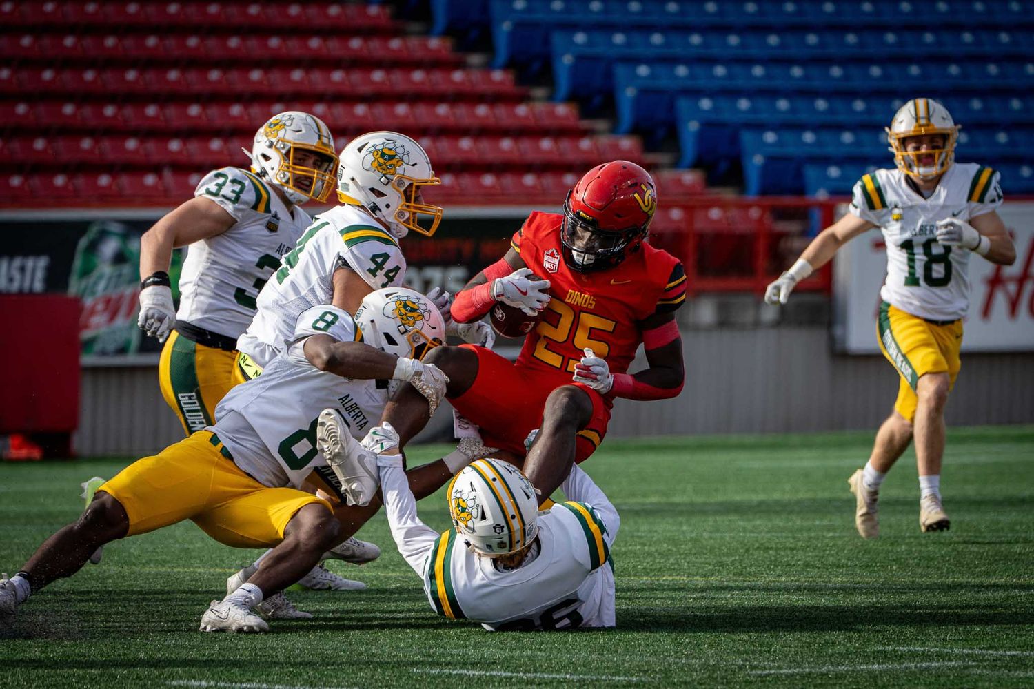Intense football tackle between players in red and gold uniforms during game.
