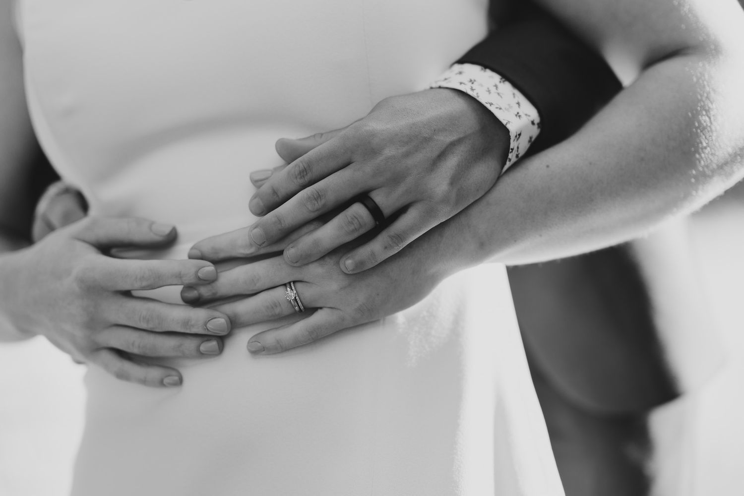 A black and white photo showing hands with wedding rings exchanging tender touches and gestures.
