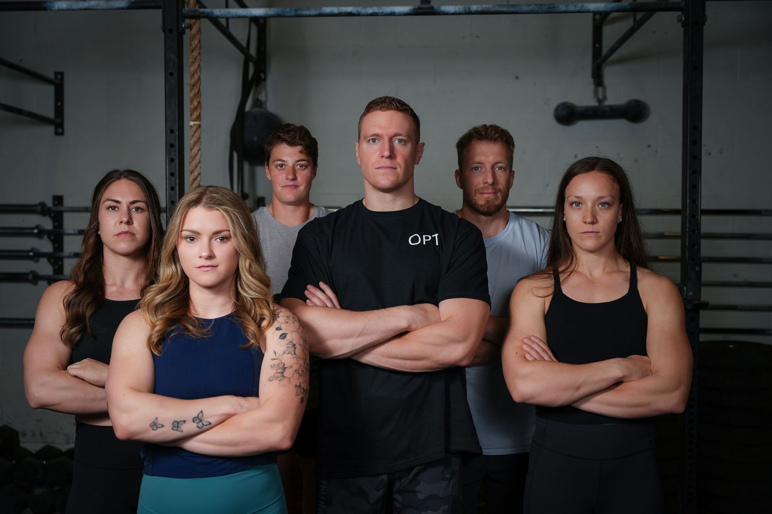 Group fitness photo of team members posing with crossed arms in gym setting.