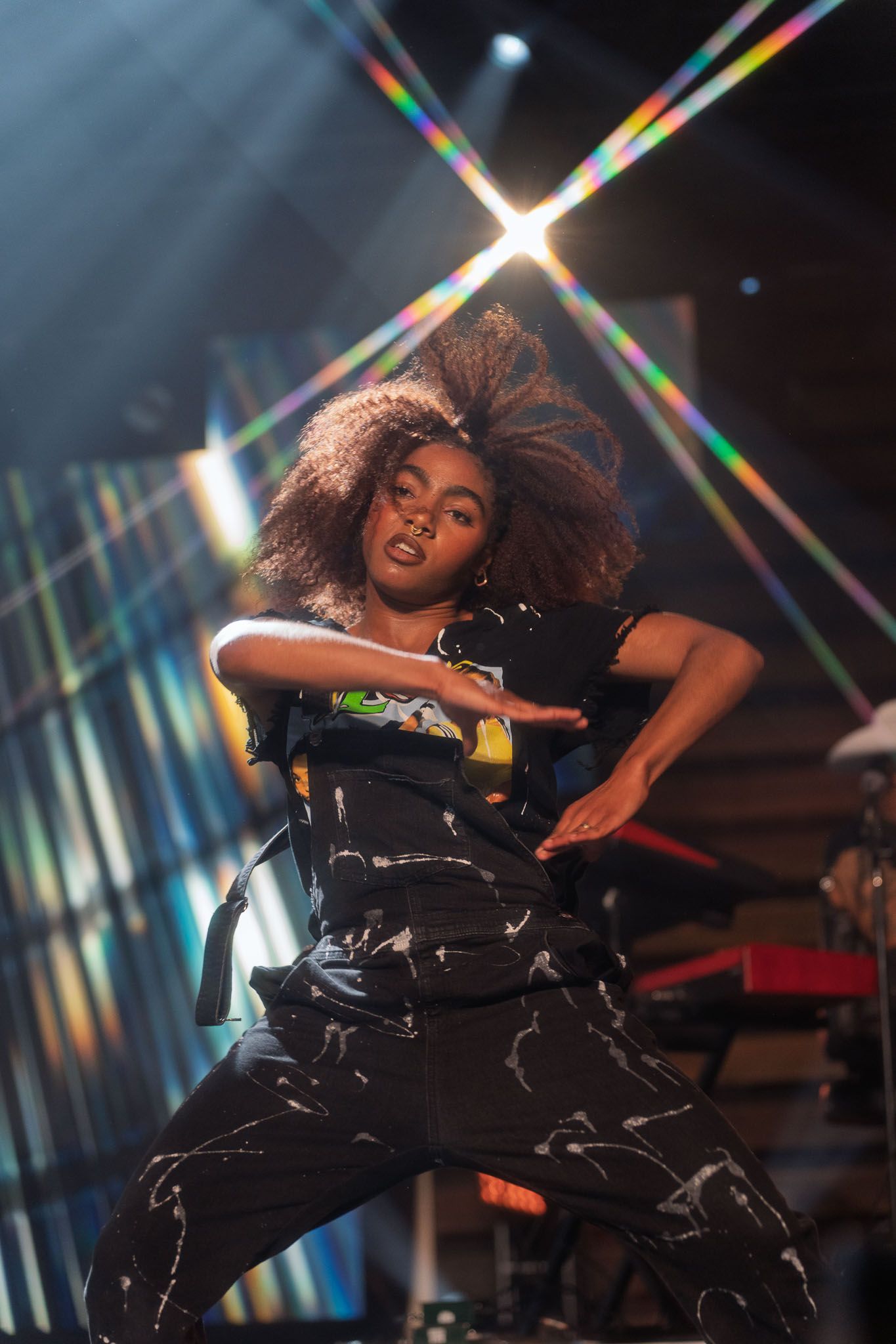 Performer in black outfit dancing energetically under prismatic stage lights.