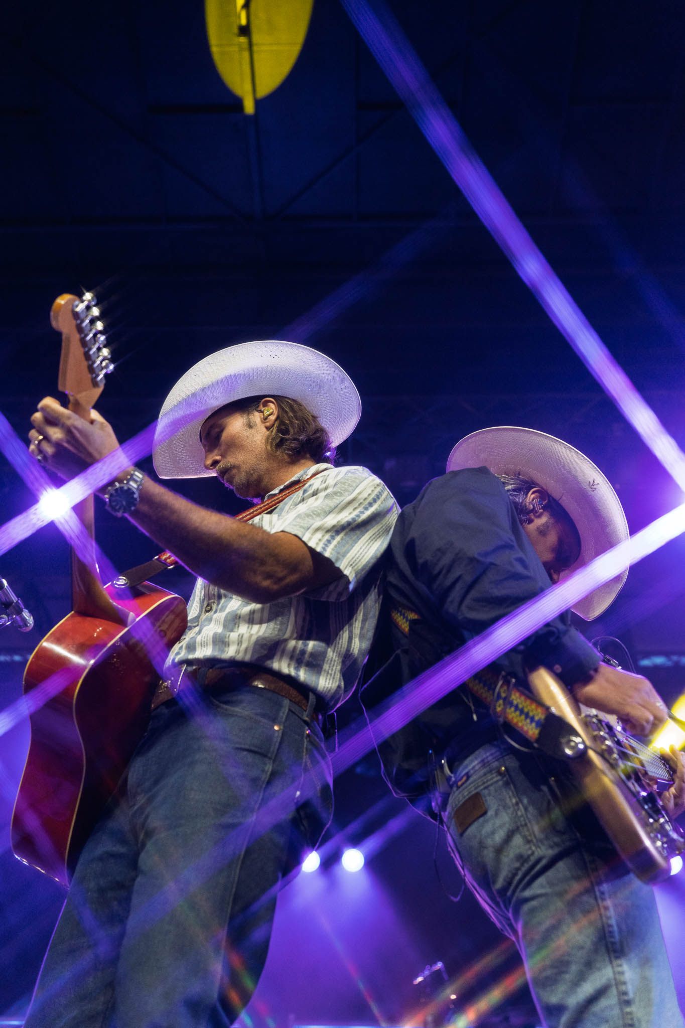 Country musicians in cowboy hats perform under purple stage lighting at night.