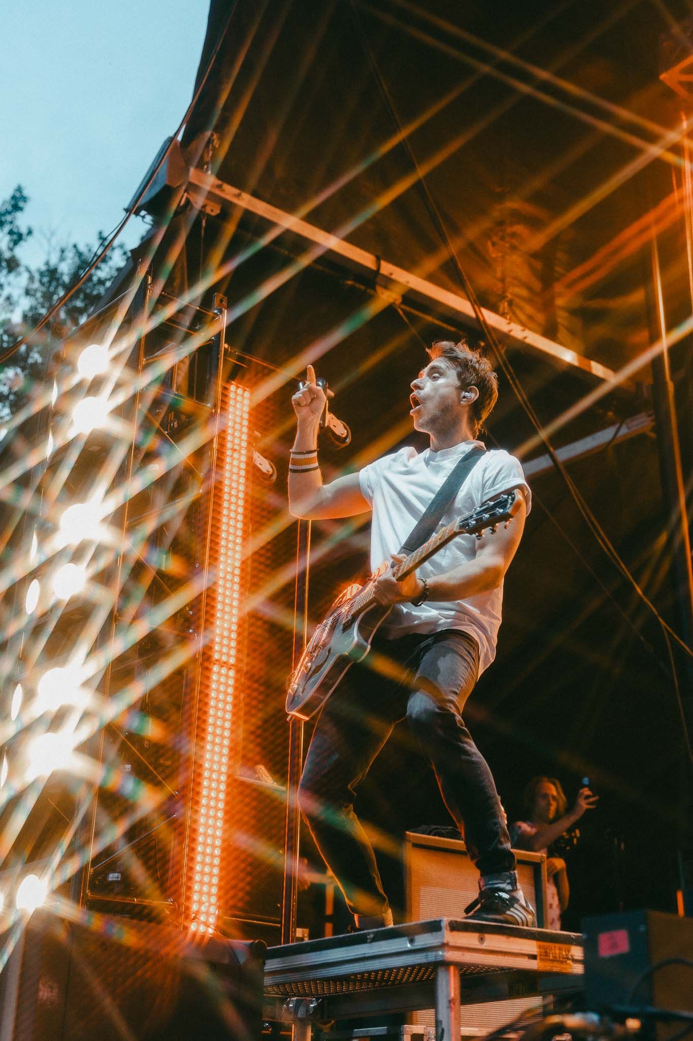 Energetic performer jumping on stage with orange lighting and dramatic lens flares.