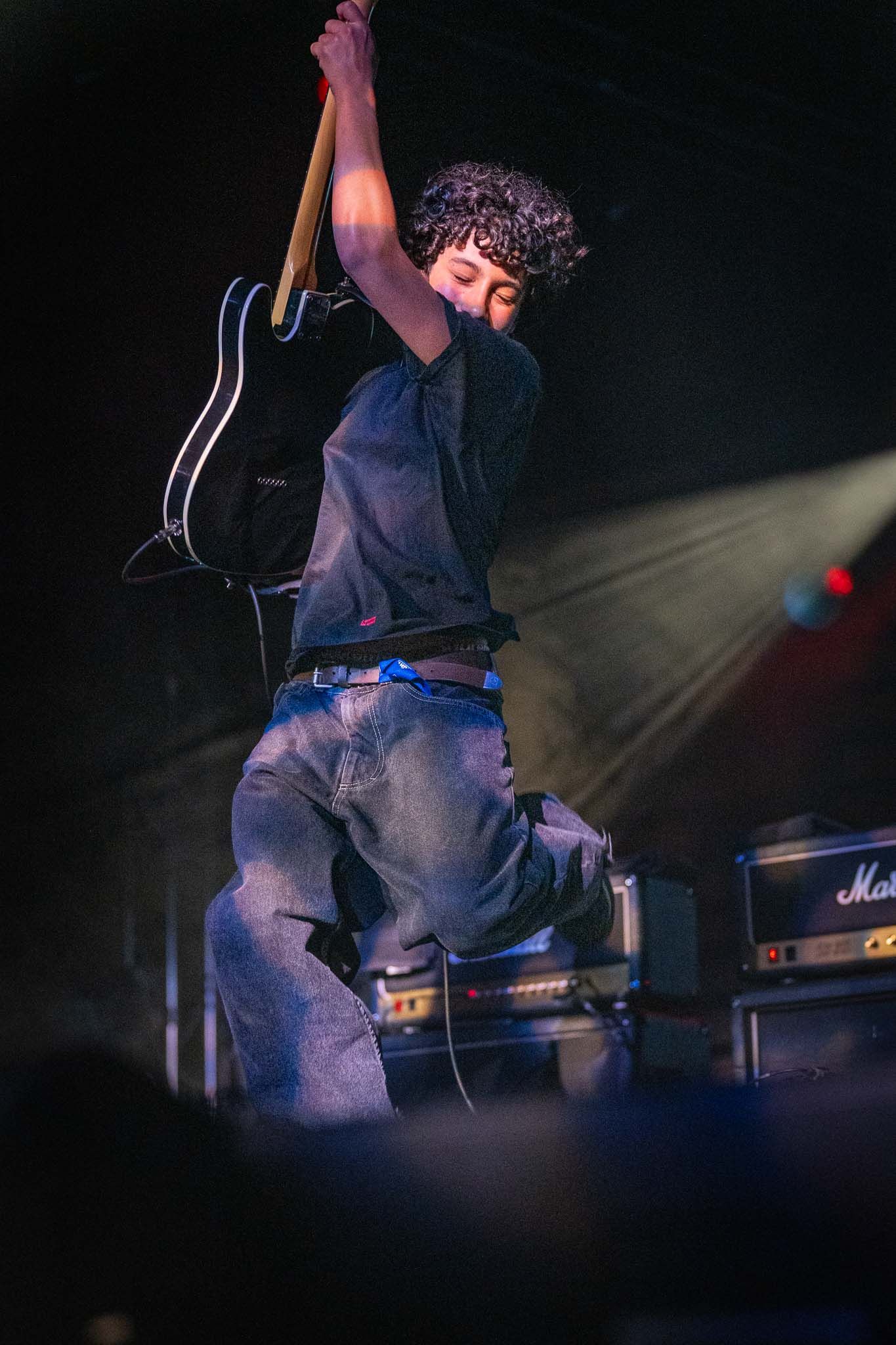 Roman Morello in dark clothing jumping on stage during dramatic concert lighting.