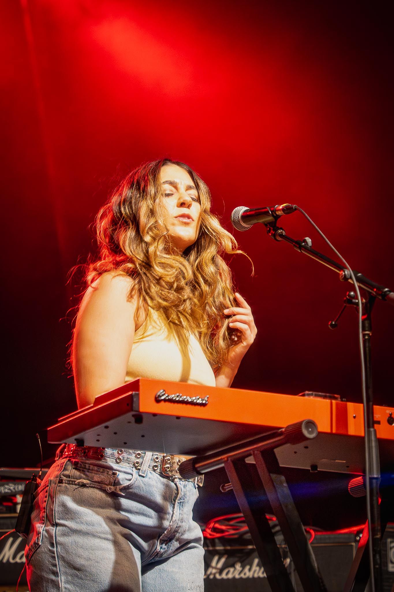 Musician plays keyboard under dramatic red stage lighting during live performance.