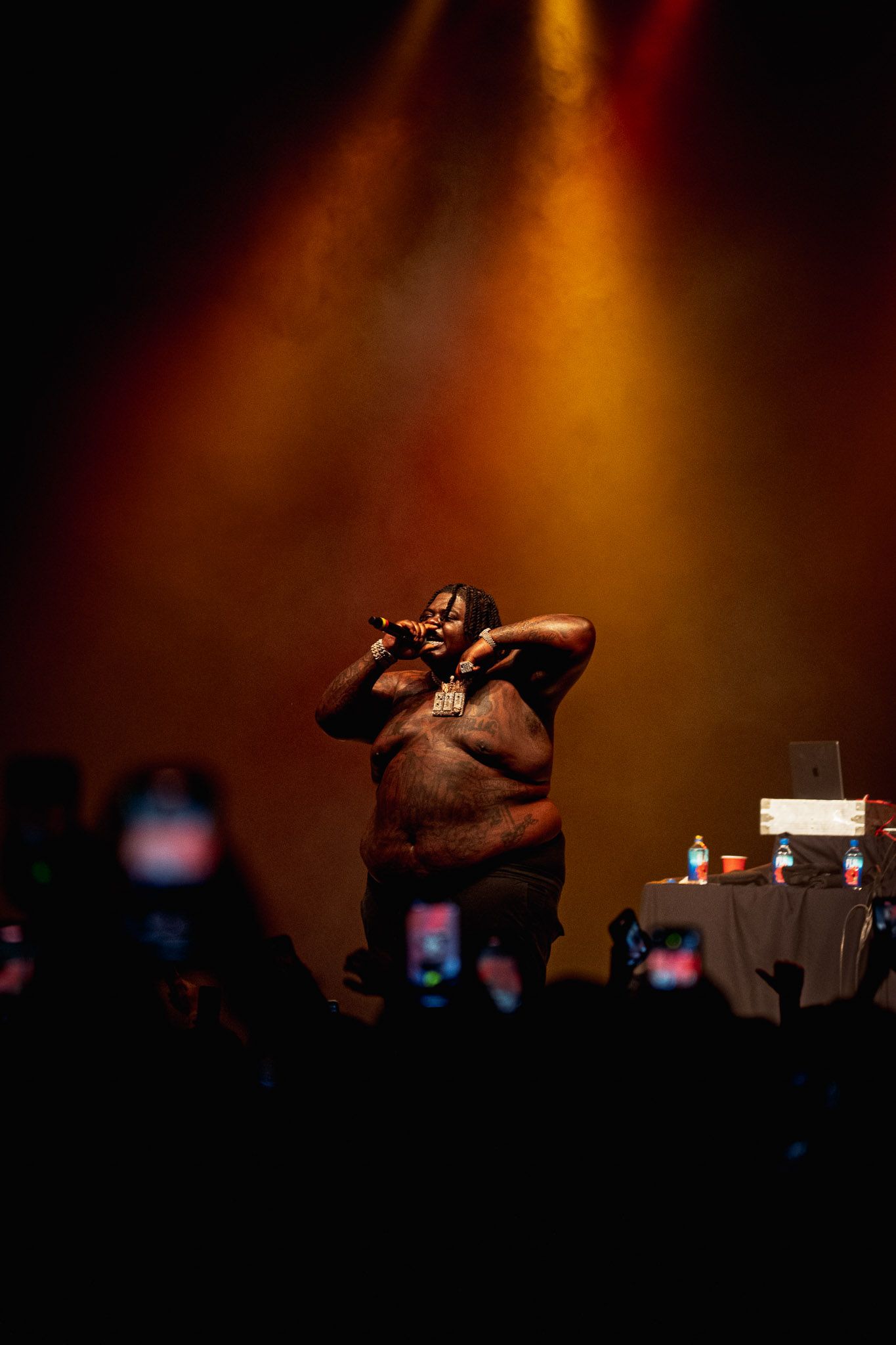 Silhouetted rapper BigXthaPlug figures against warm orange stage lighting at concert venue.