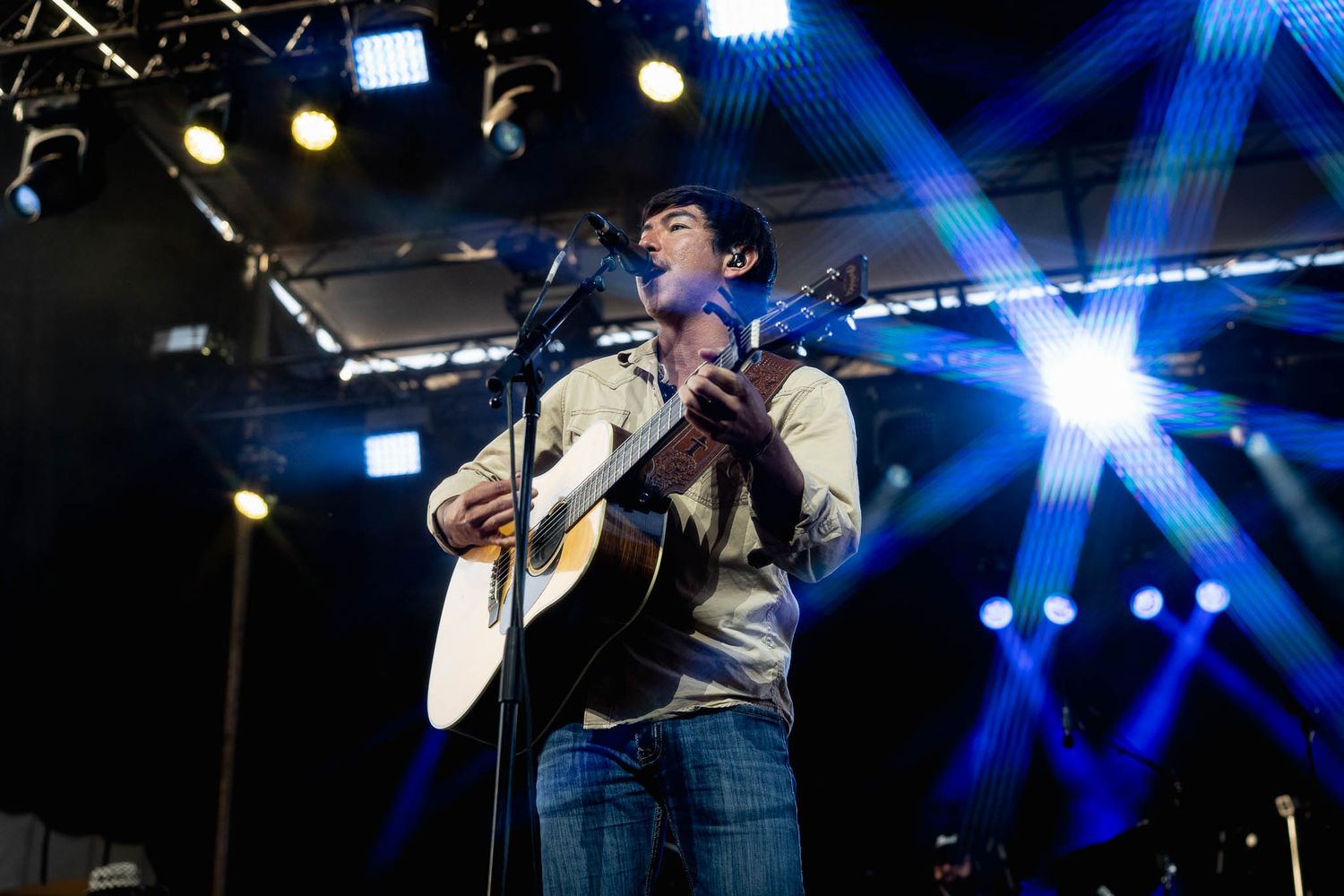 Concert performer plays acoustic guitar on stage with dramatic blue lighting effects.