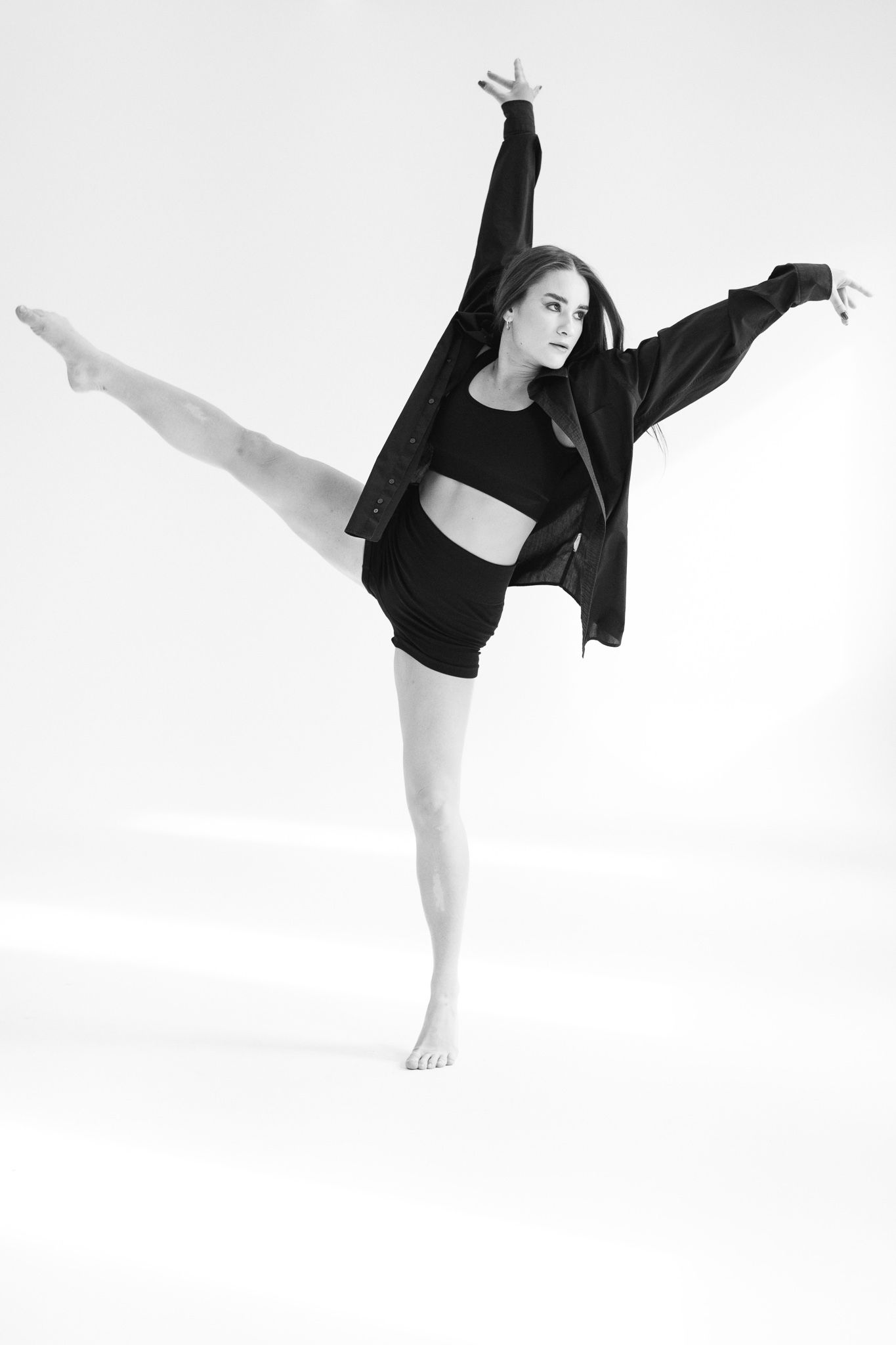 Dancer in black outfit performs expressive movements against minimalist white background.