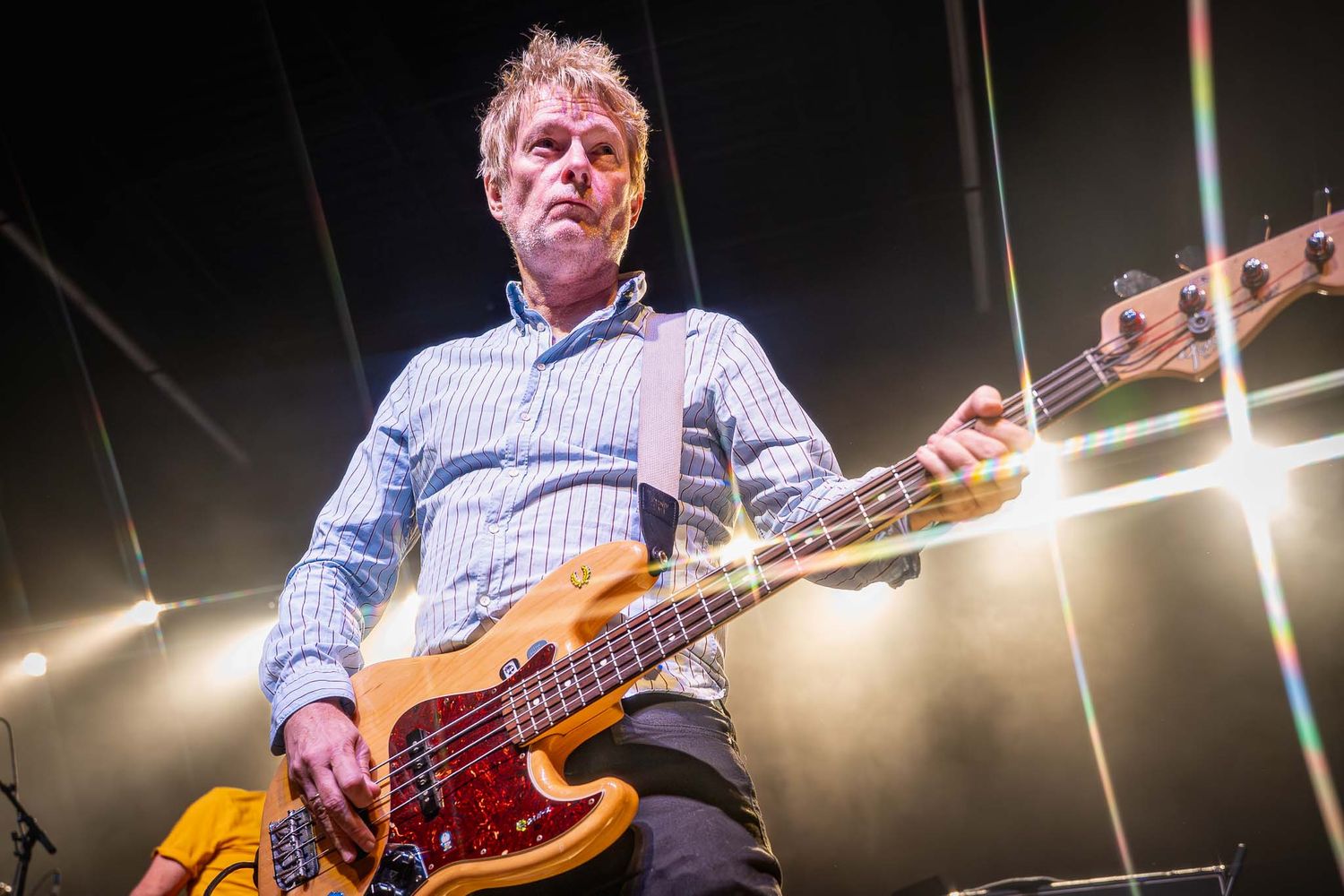 Musician playing bass guitar under bright stage lights during performance.