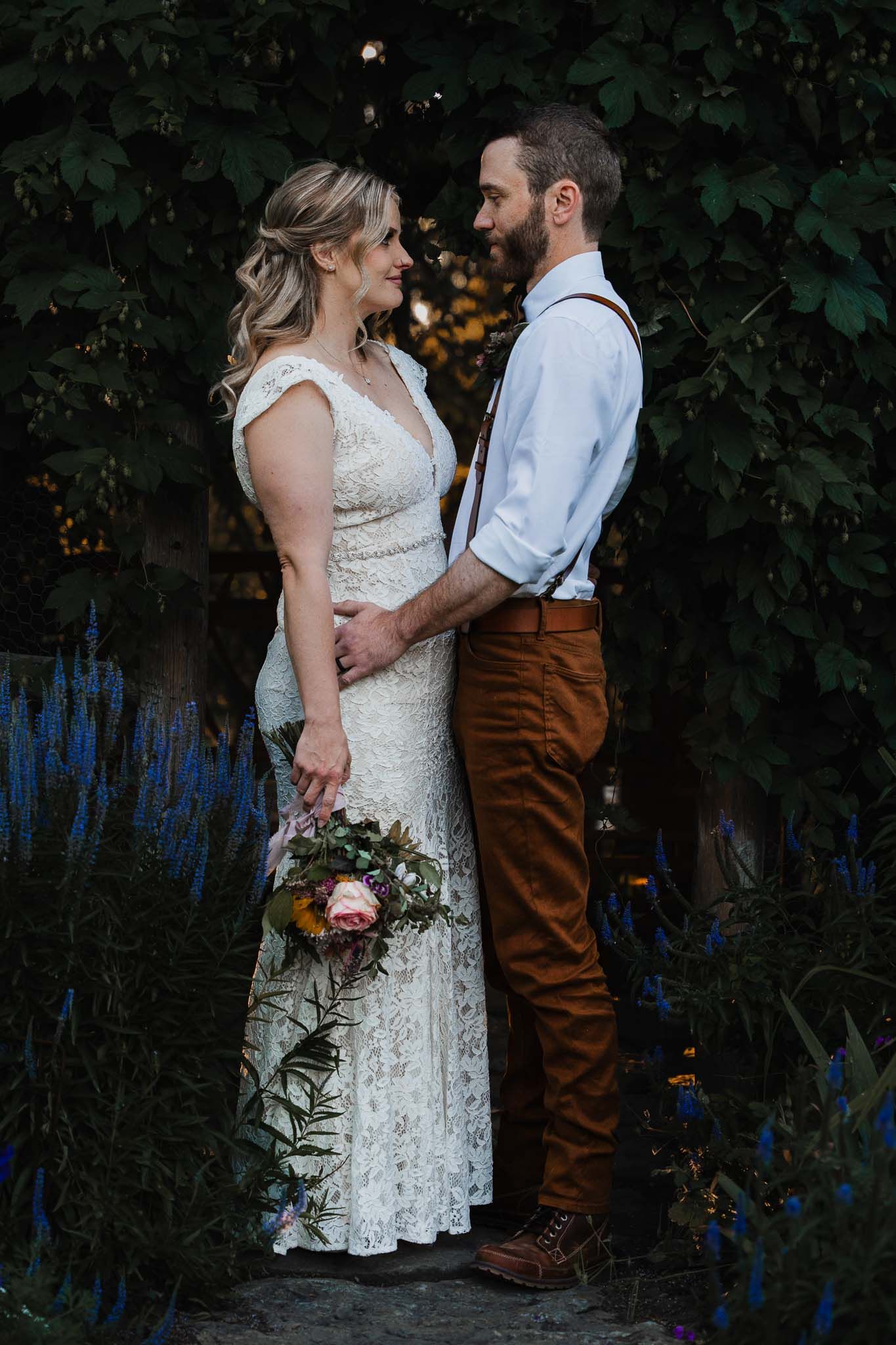 Couple in wedding attire shares intimate moment in garden setting.