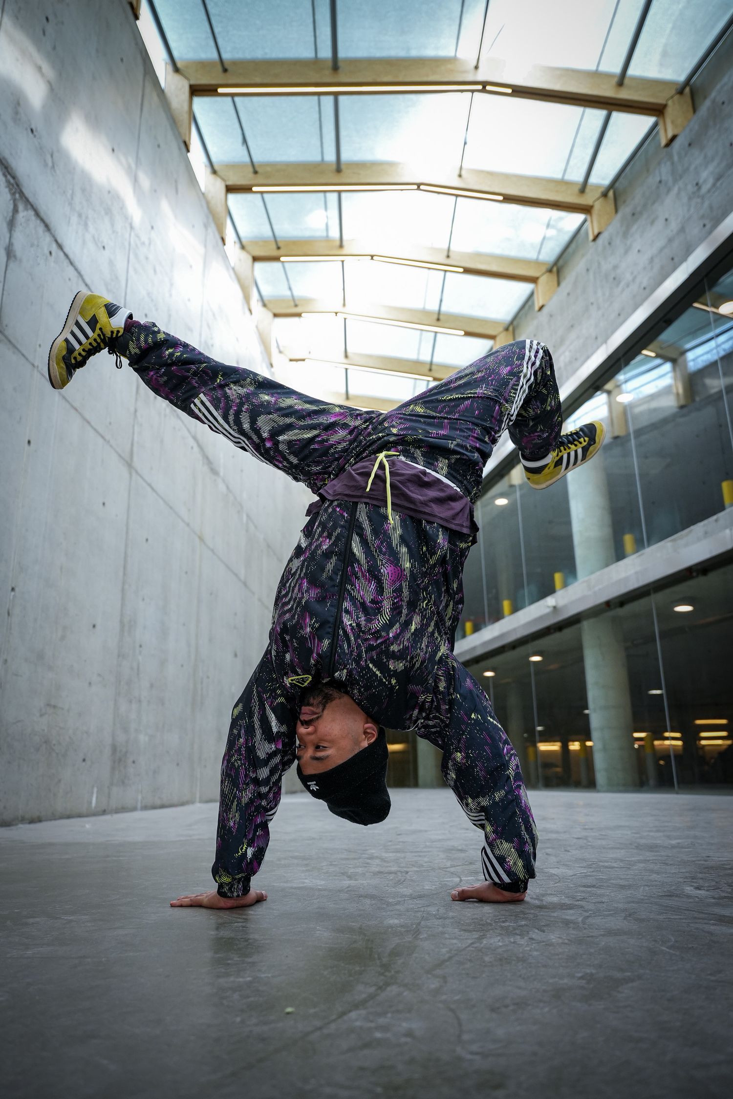 Dancer in patterned outfit performs freeze move in concrete indoor space.