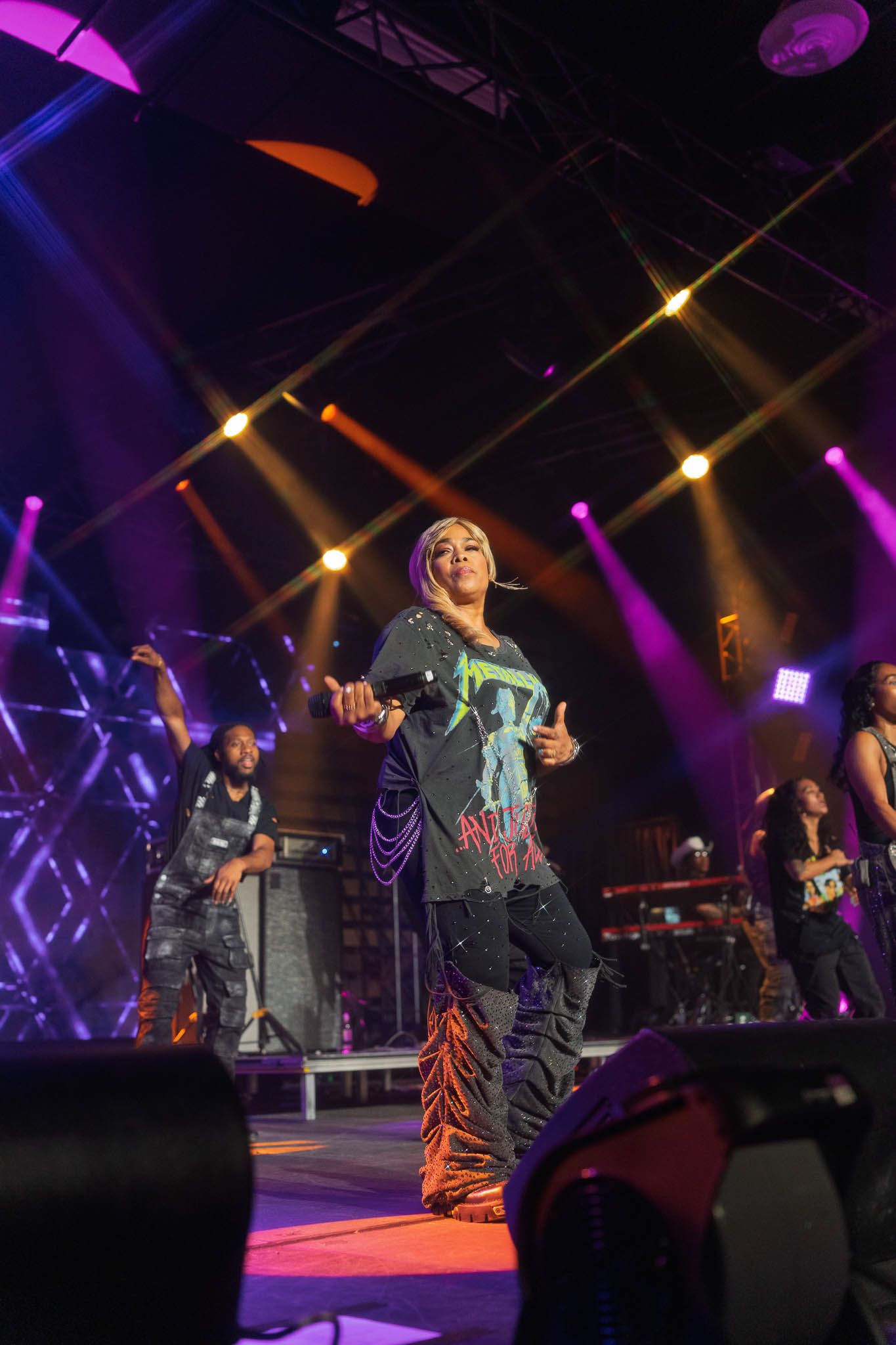 Wide shot of concert stage with colorful lighting and multiple performers in action.