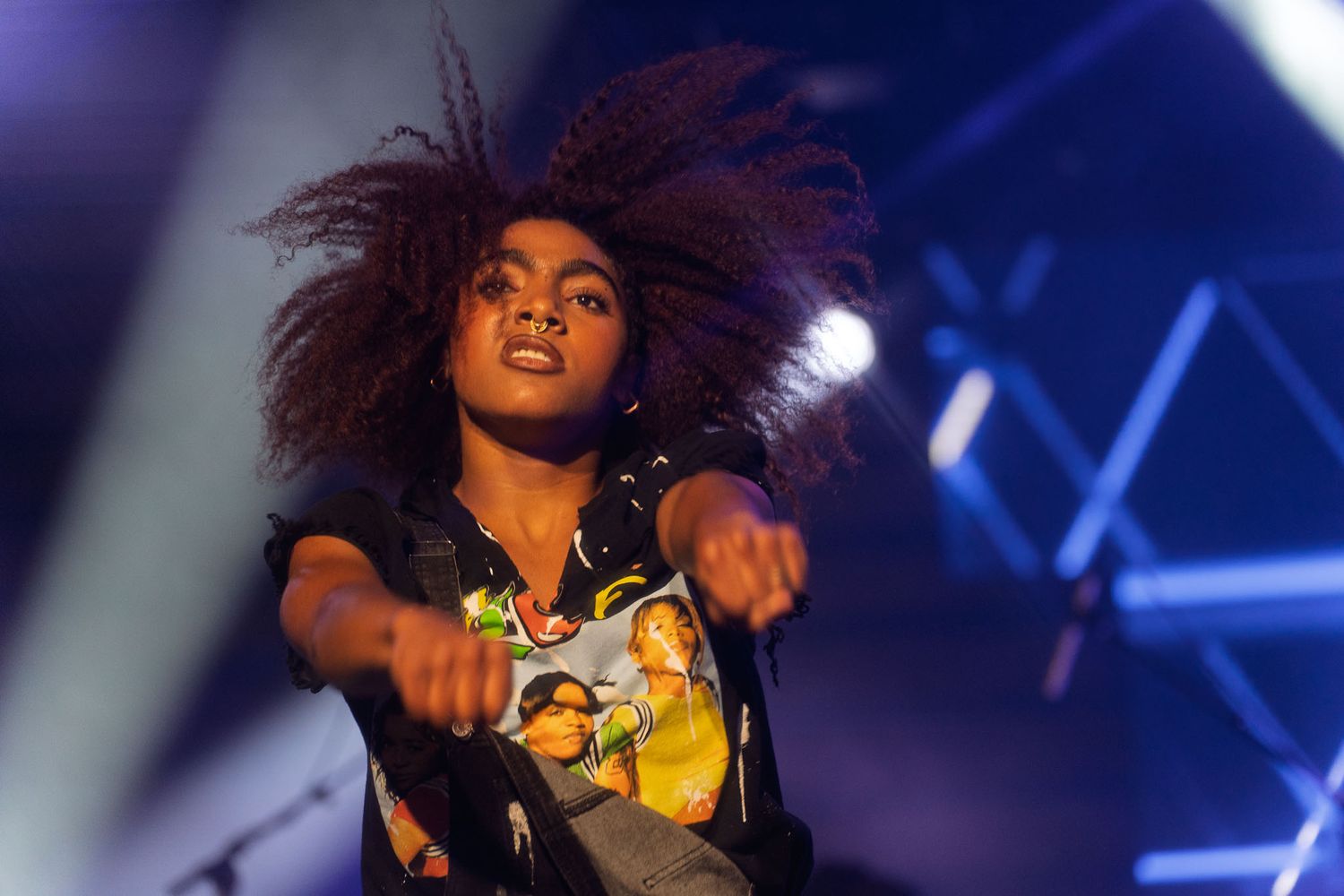 Energetic performer with natural hair dances on stage under dramatic concert lighting.