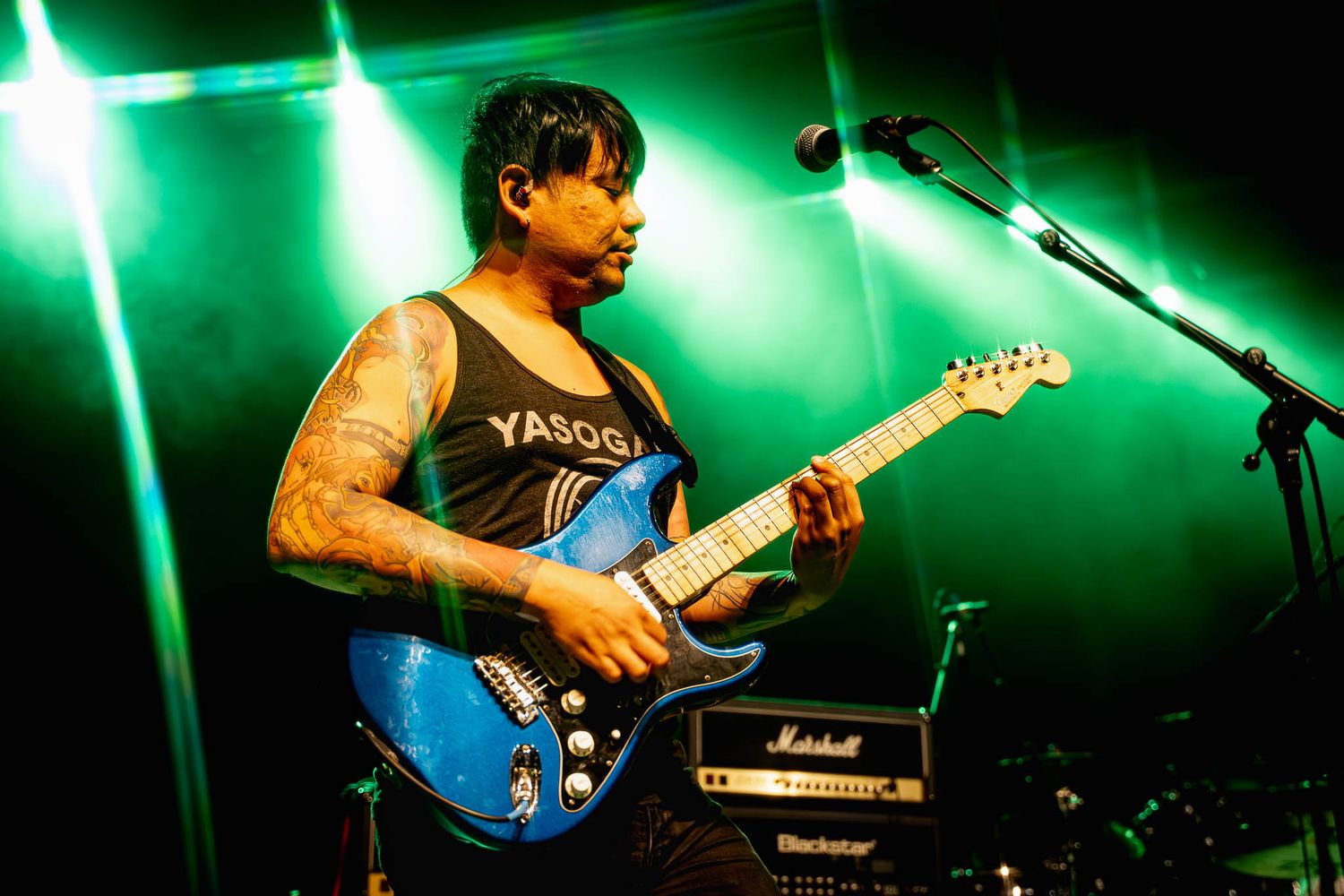 Guitarist performs with blue guitar under dramatic green stage lighting at rock concert.