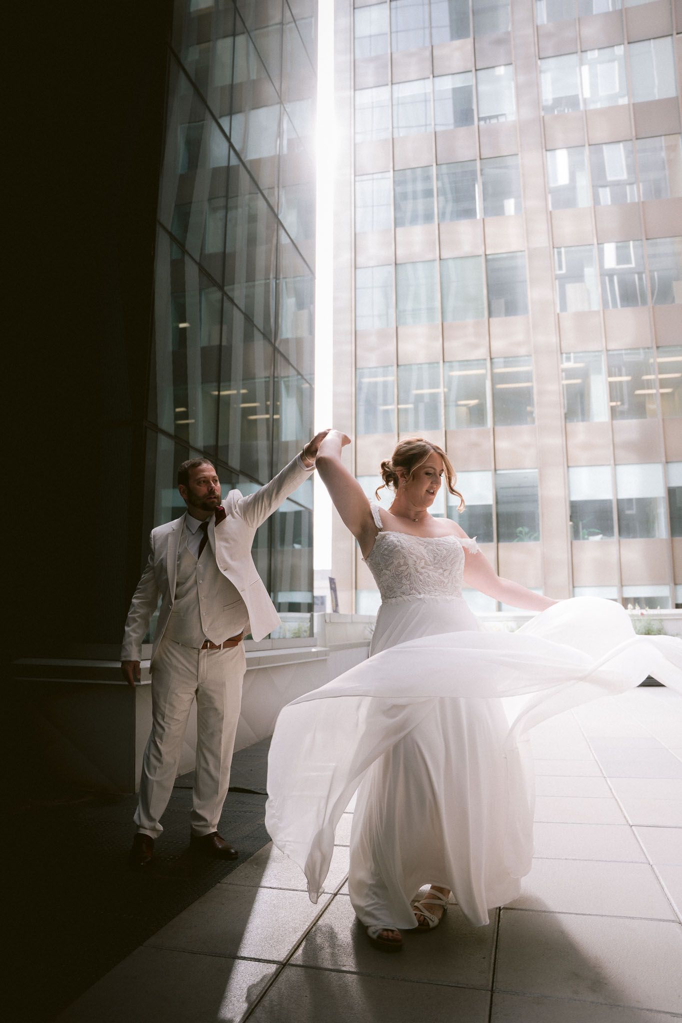 Artistic wedding photos in a modern building with dramatic backlighting and flowing white dress.