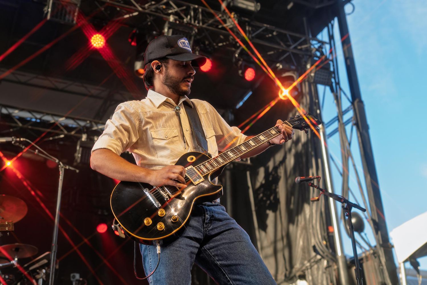Musicians performing with guitars on outdoor stage during daytime festival.
