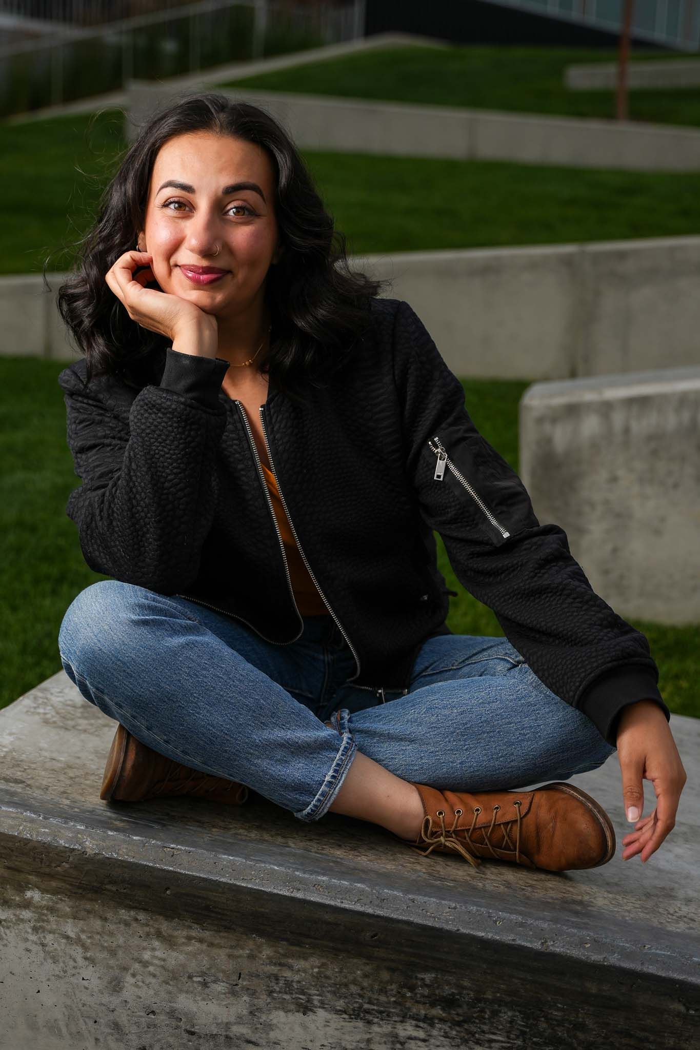 Relaxed pose on concrete steps wearing black bomber jacket and classic denim.