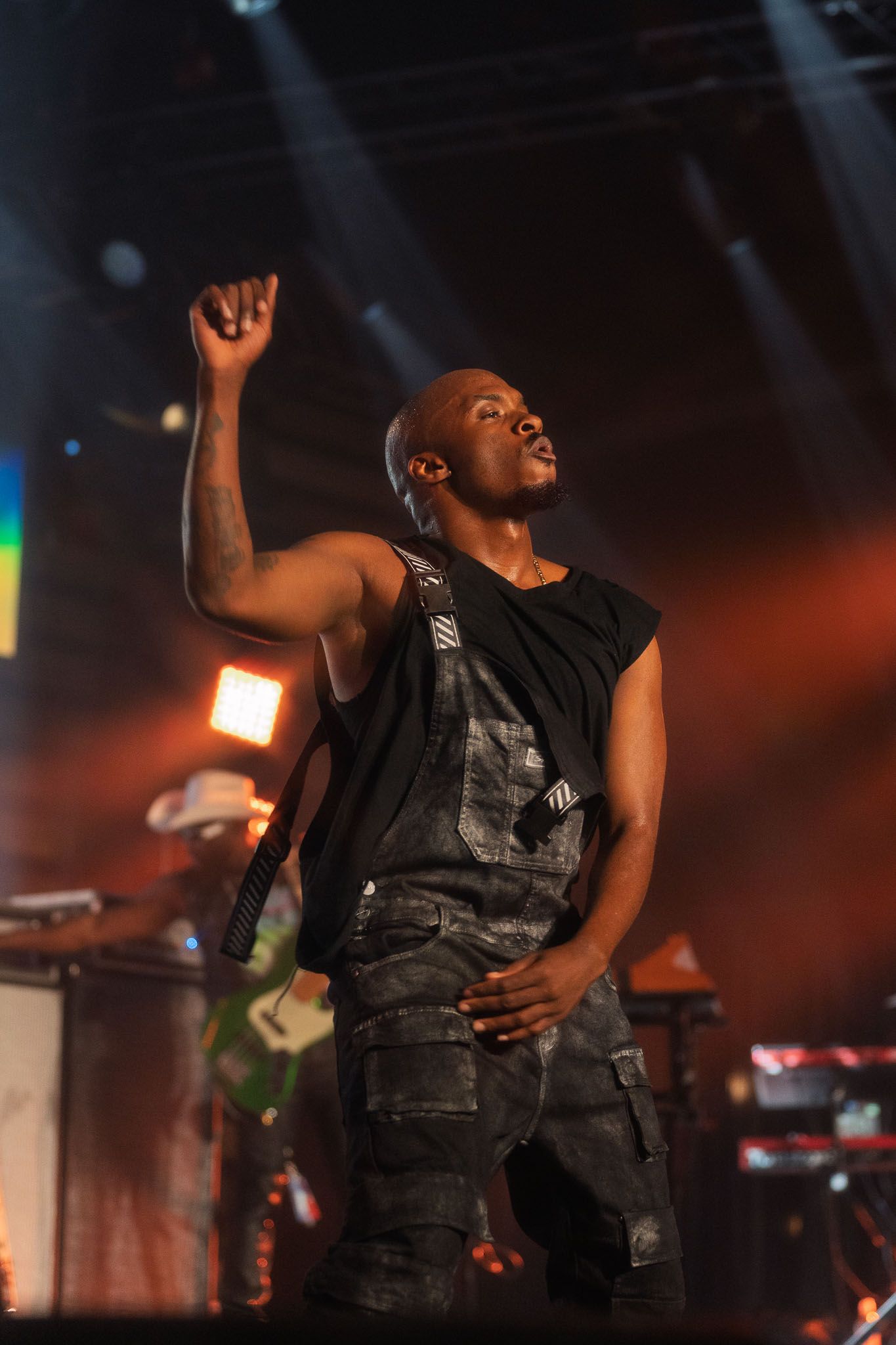 Performers in dark vests moving dynamically on stage with orange lighting effects.