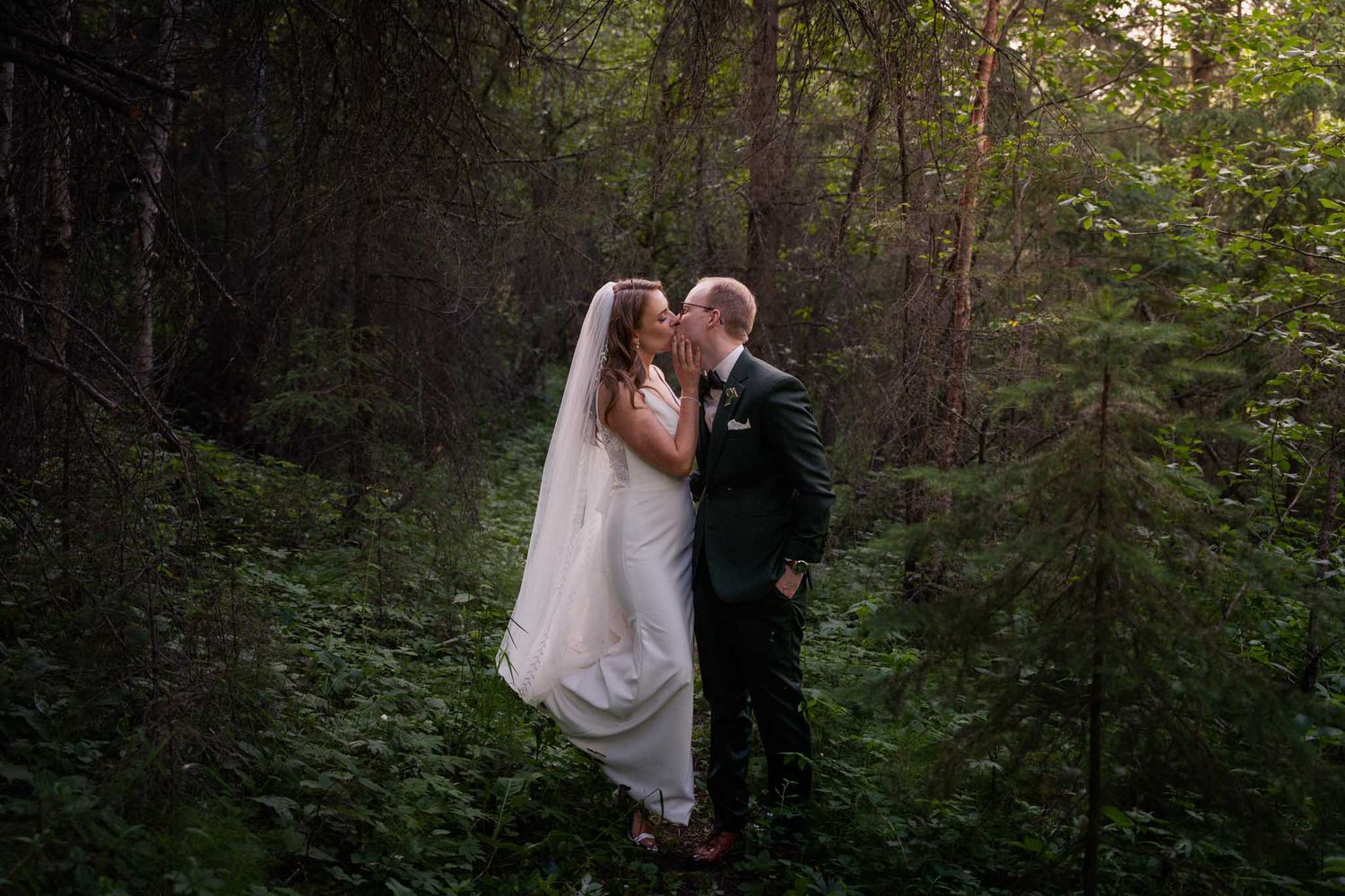 A couple poses for romantic wedding photos in a lush green forest setting.