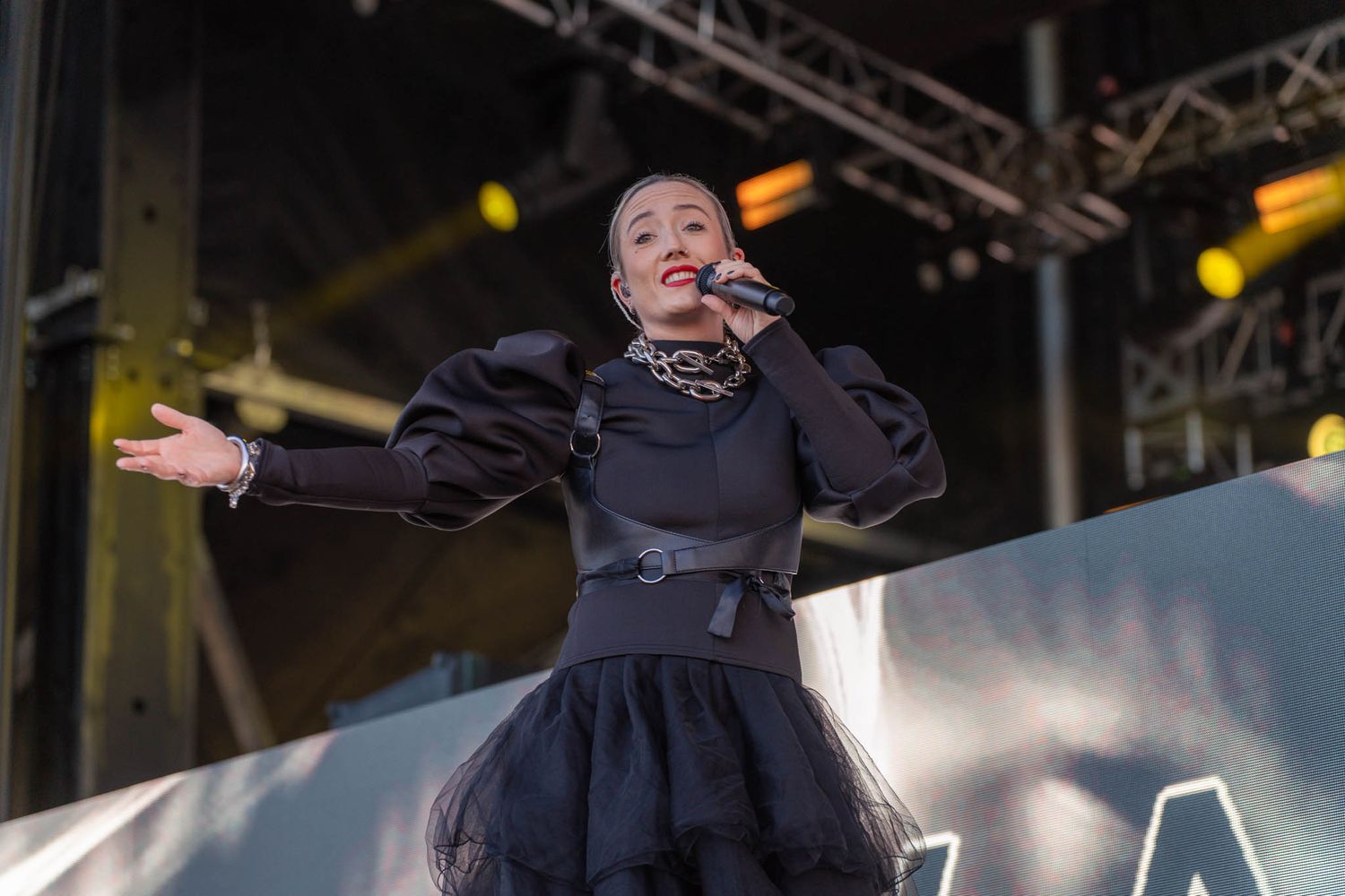 Musician performing passionately on stage with dramatic lighting and concert equipment visible in background.