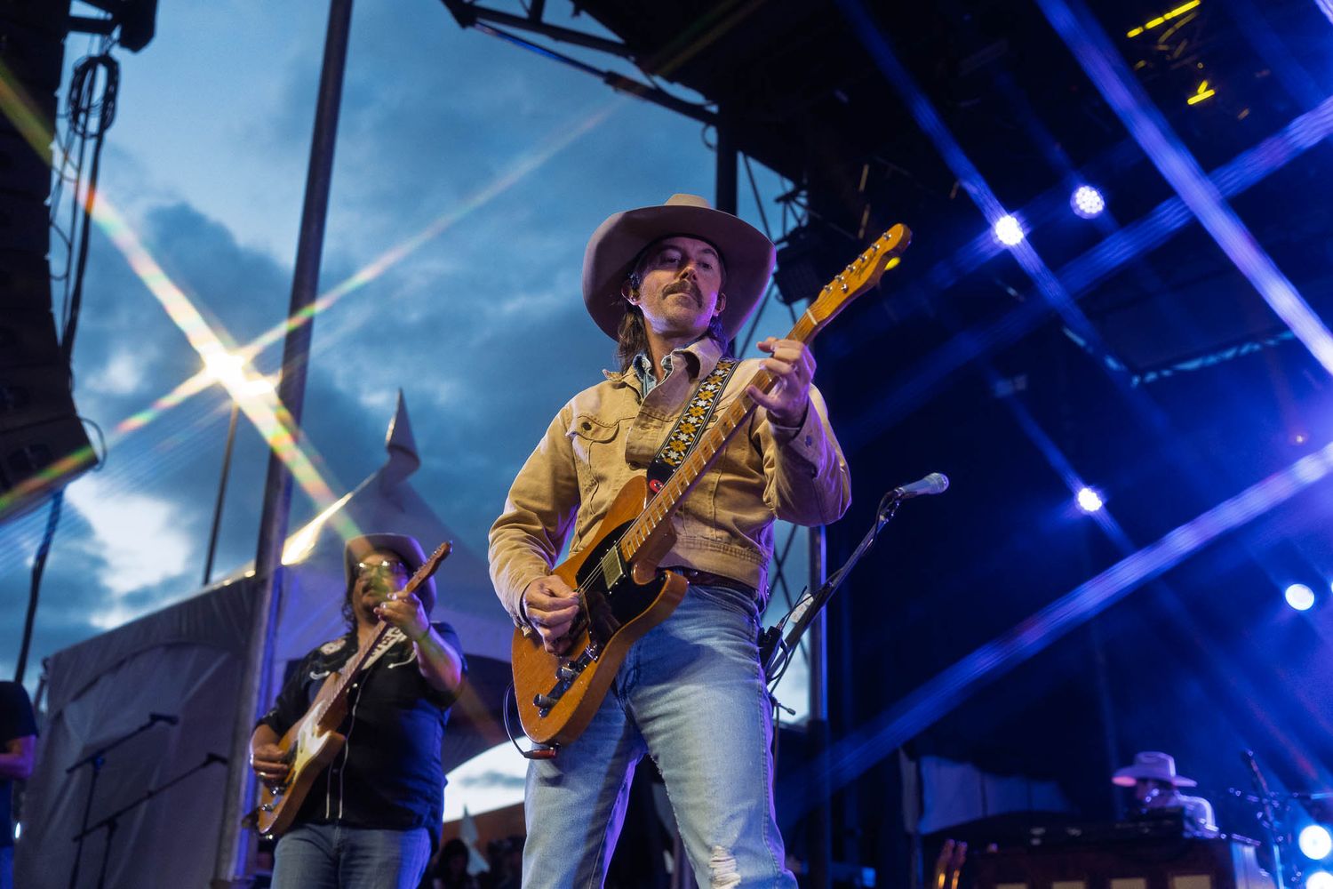 Musicians perform on stage with dramatic blue lighting and lens flares.