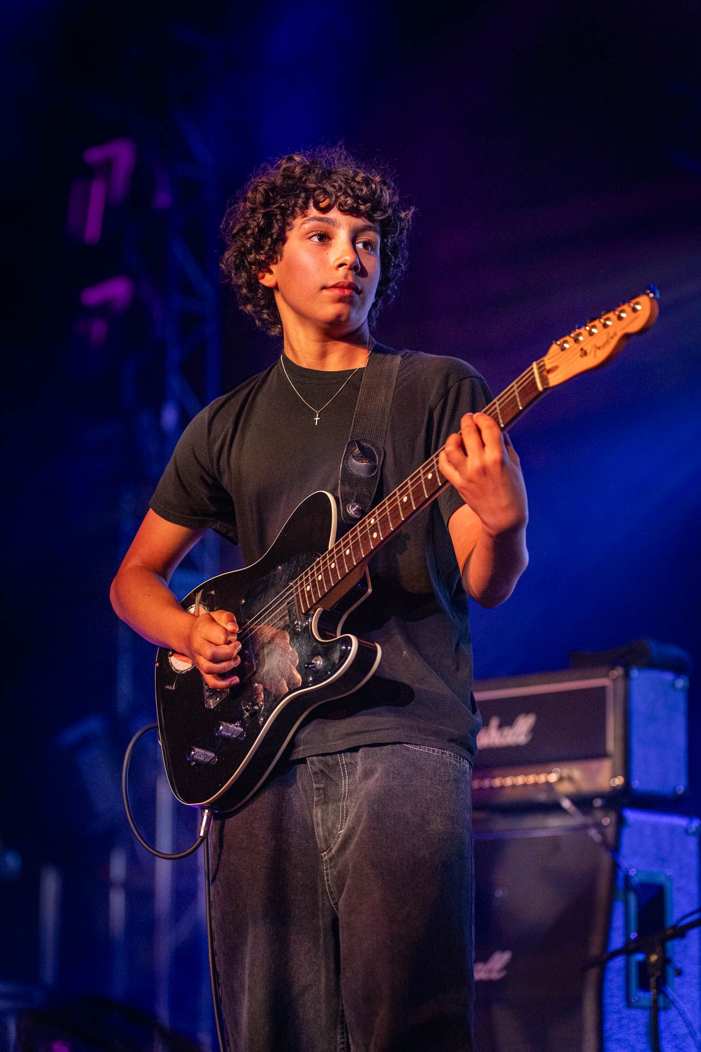 Roman Morello playing electric guitar on stage with blue lighting effects.
