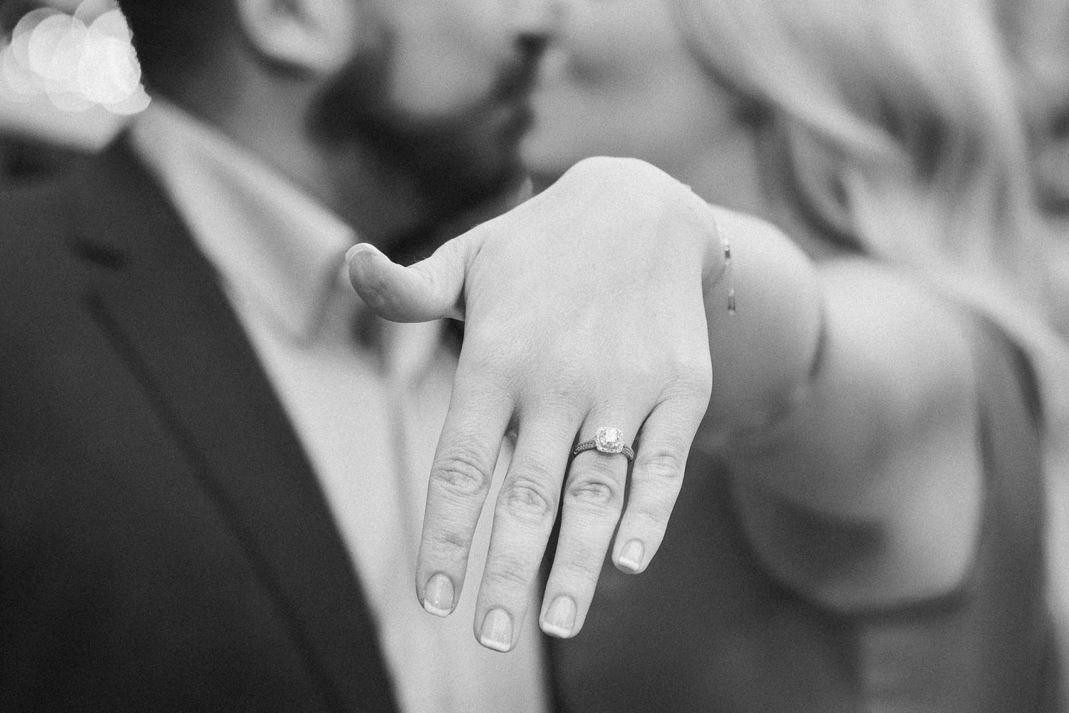 Close-up details of wedding rings and hands in black and white photography.