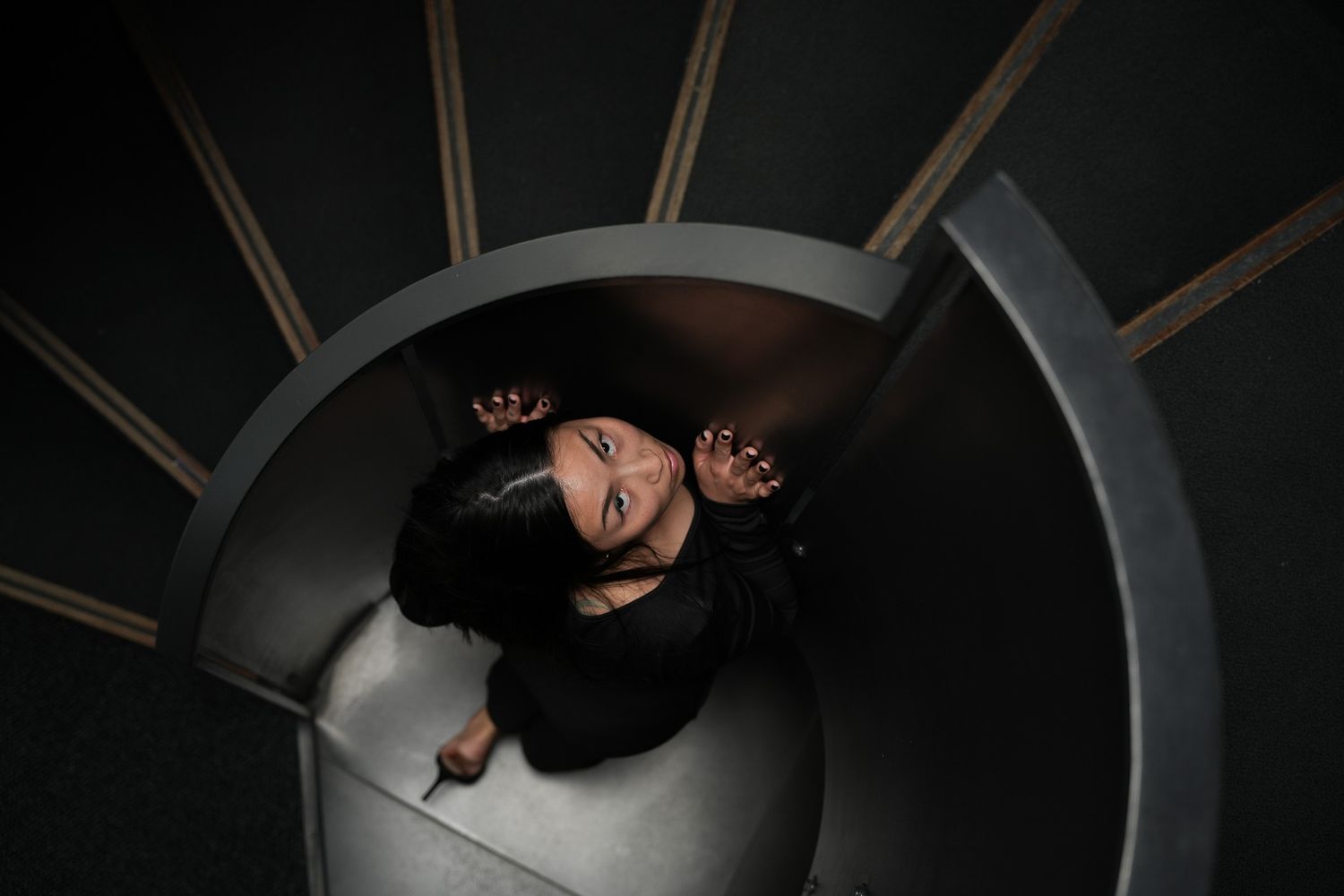 Dramatic overhead view of a figure in dark lighting with curved architectural elements.