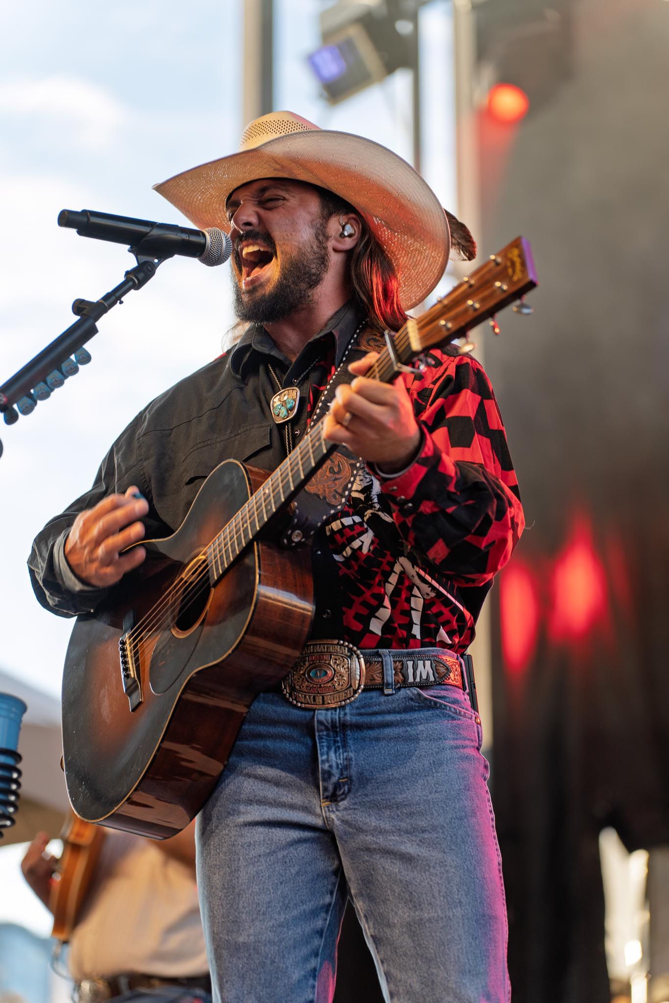Country artist Ian Munsick performing with acoustic guitars on stage wearing cowboy hats and jeans under red stage lights.
