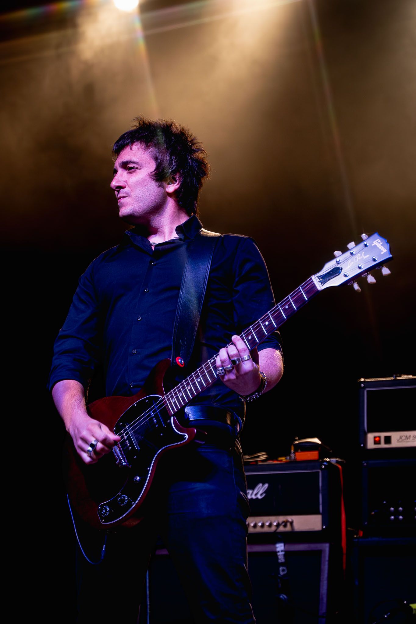 Guitarist in dark blue shirt performing on stage under dramatic concert lighting.
