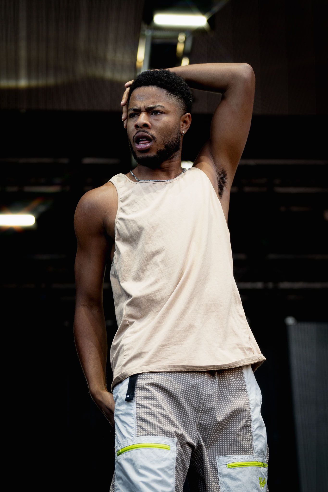 Performer in white tank top and cargo pants strikes dramatic pose on stage during show.
