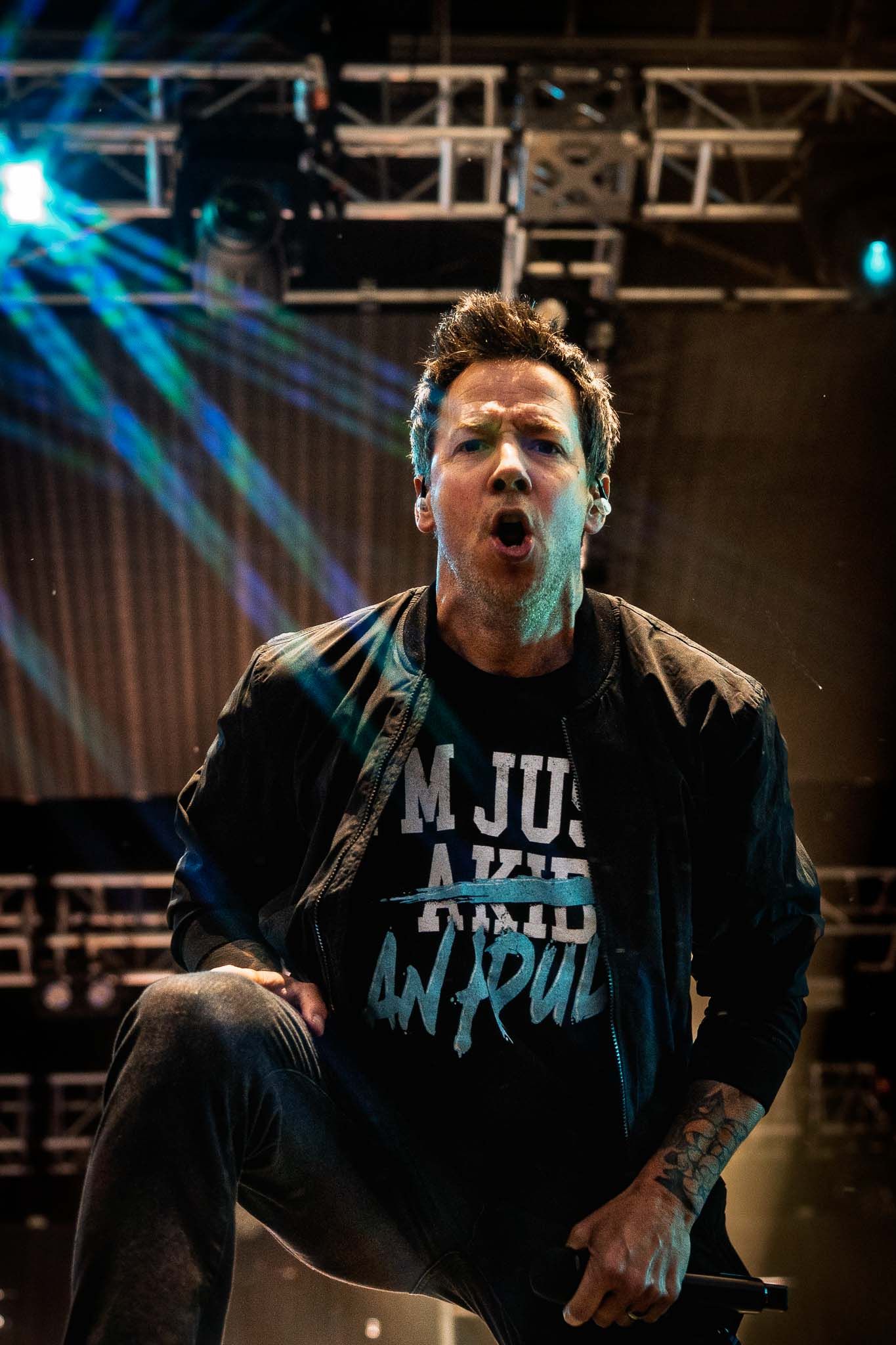 Simple Plan  in black attire singing passionately on dimly lit concert stage.