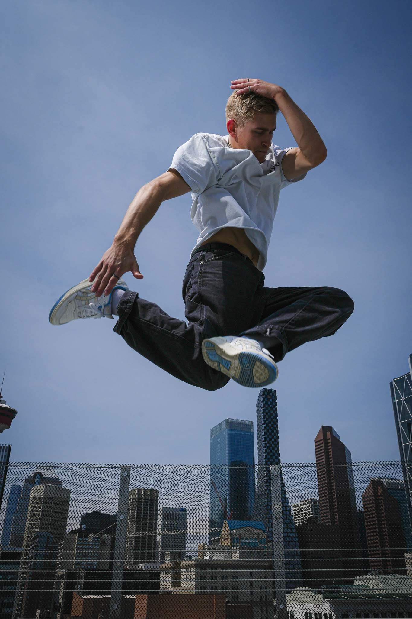 Person performs parkour jump against city skyline with blue sky background.