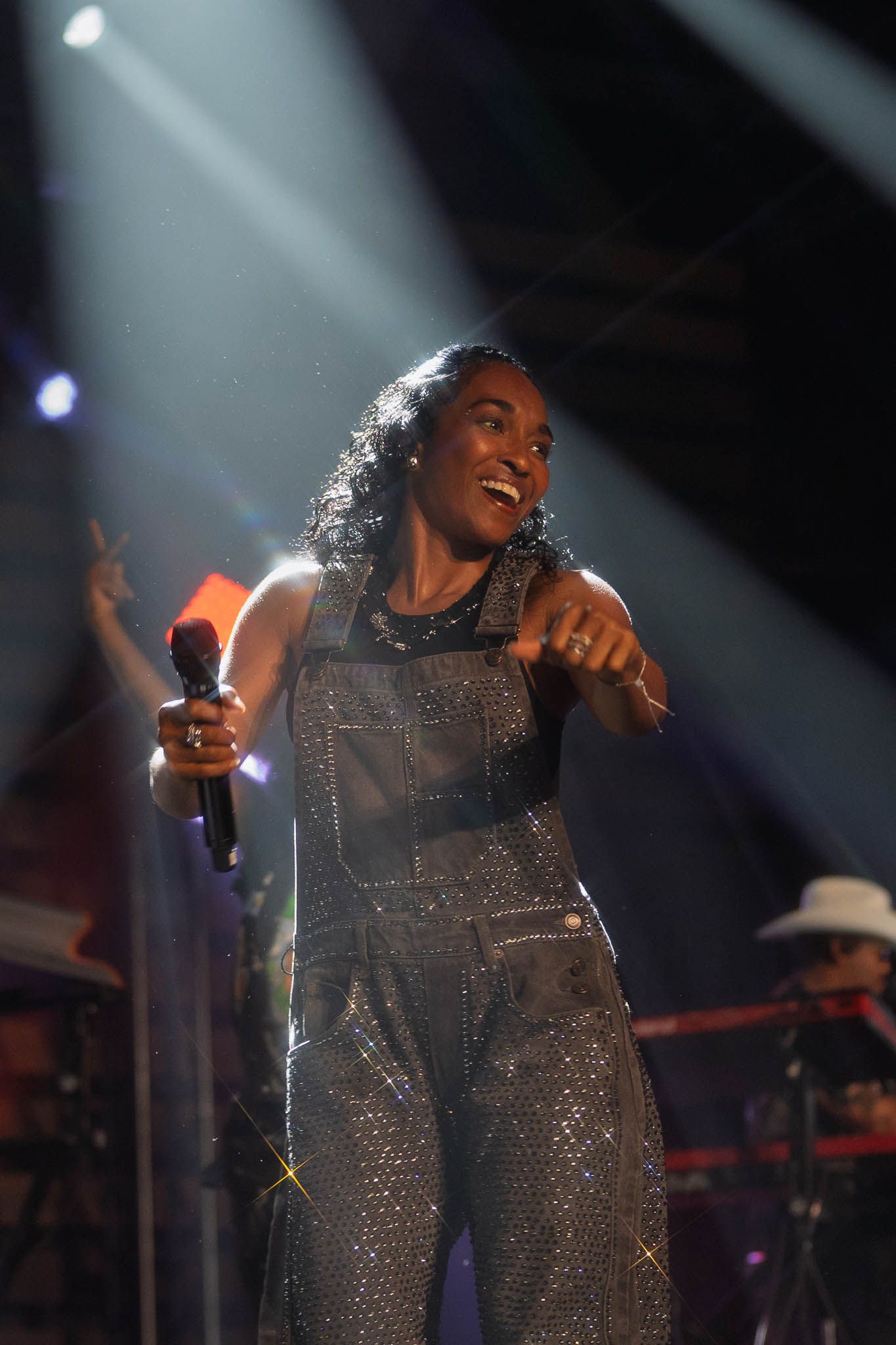 Performer in sparkling overalls singing and dancing under dramatic stage lighting.