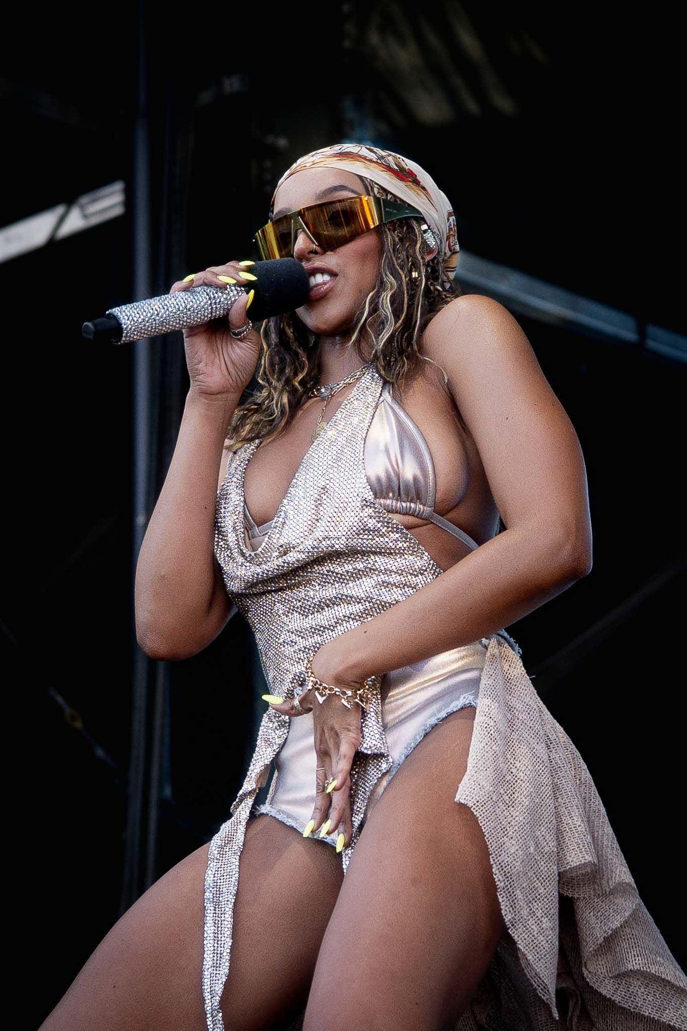 Tinashe in sparkly silver costume sings into microphone during live show.