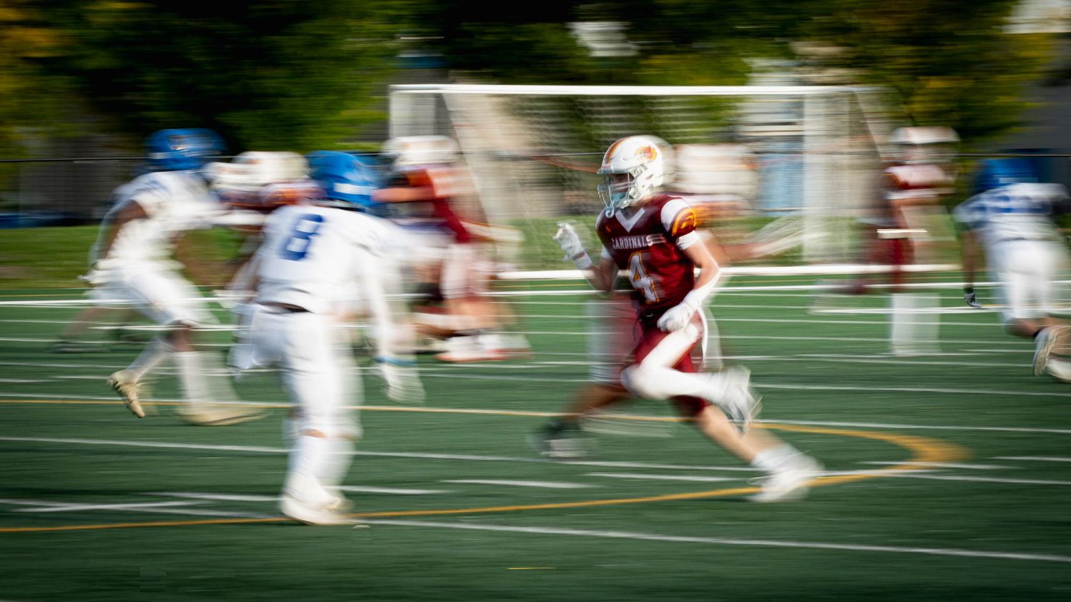 Motion blur capture of football players competing on artificial turf field.
