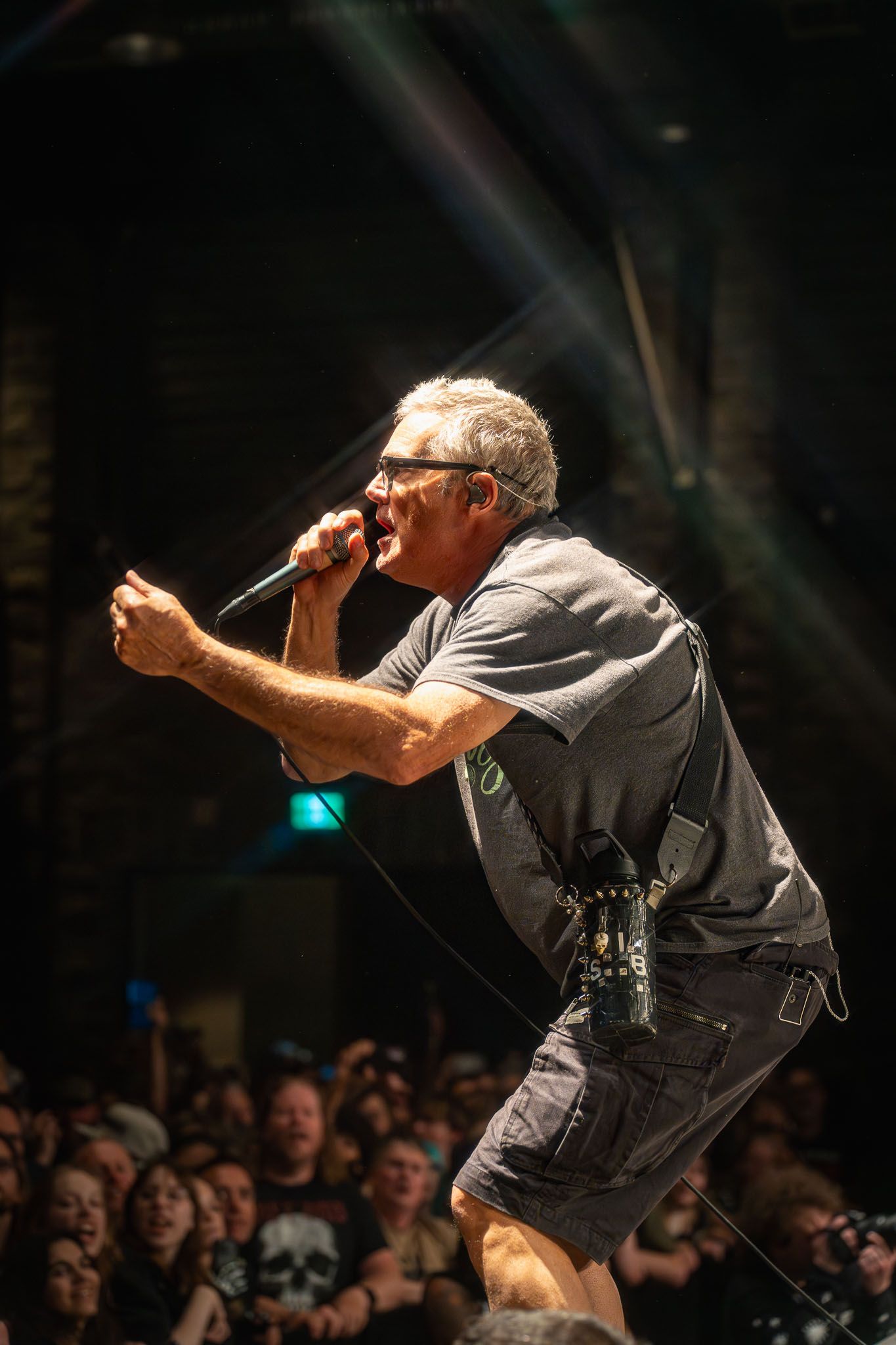 Energetic performer from The Descendents in dark clothing leaning forward while singing on stage with dramatic lighting.