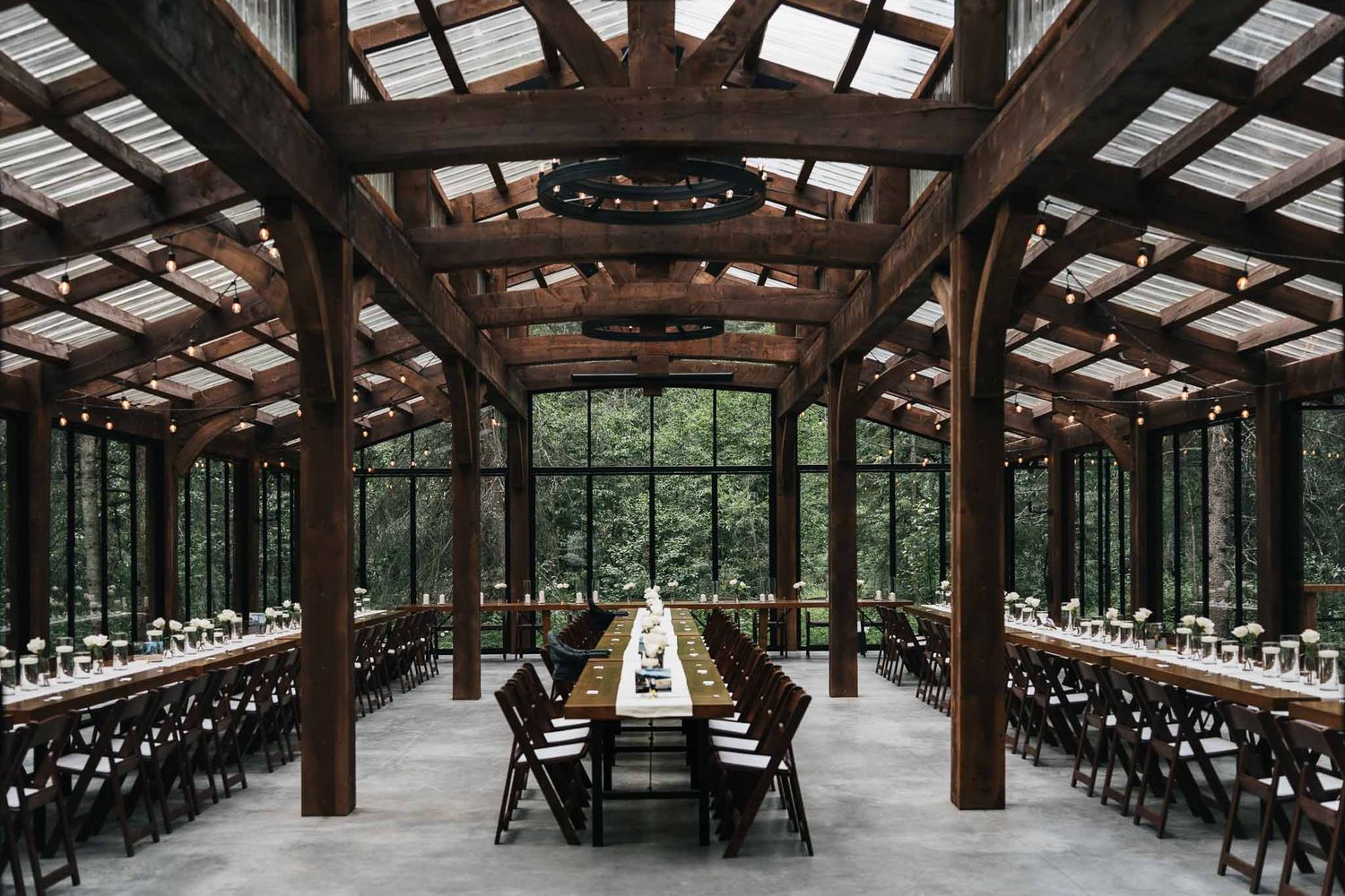 Large rustic wooden pavilion with exposed beams and rows of tables set up for a wedding reception known as The Valley Weddings