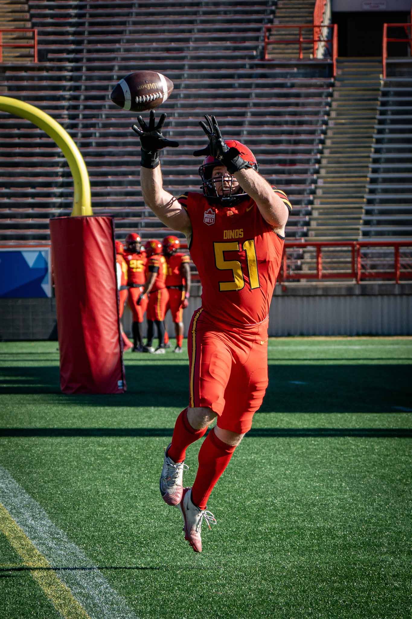 Football player in orange uniform catching ball on artificial turf field.