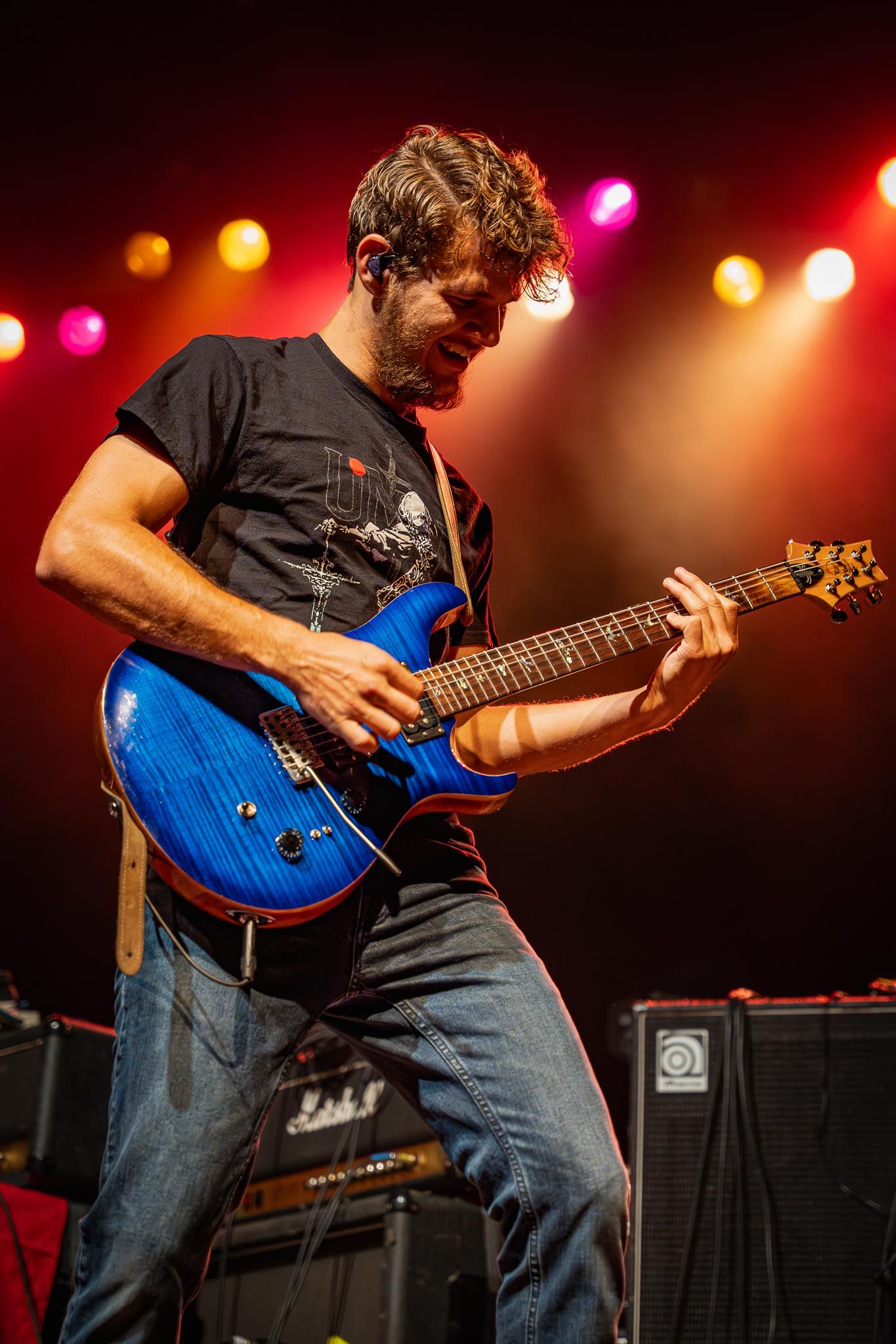 Musician playing blue electric guitar with intense focus during concert performance.