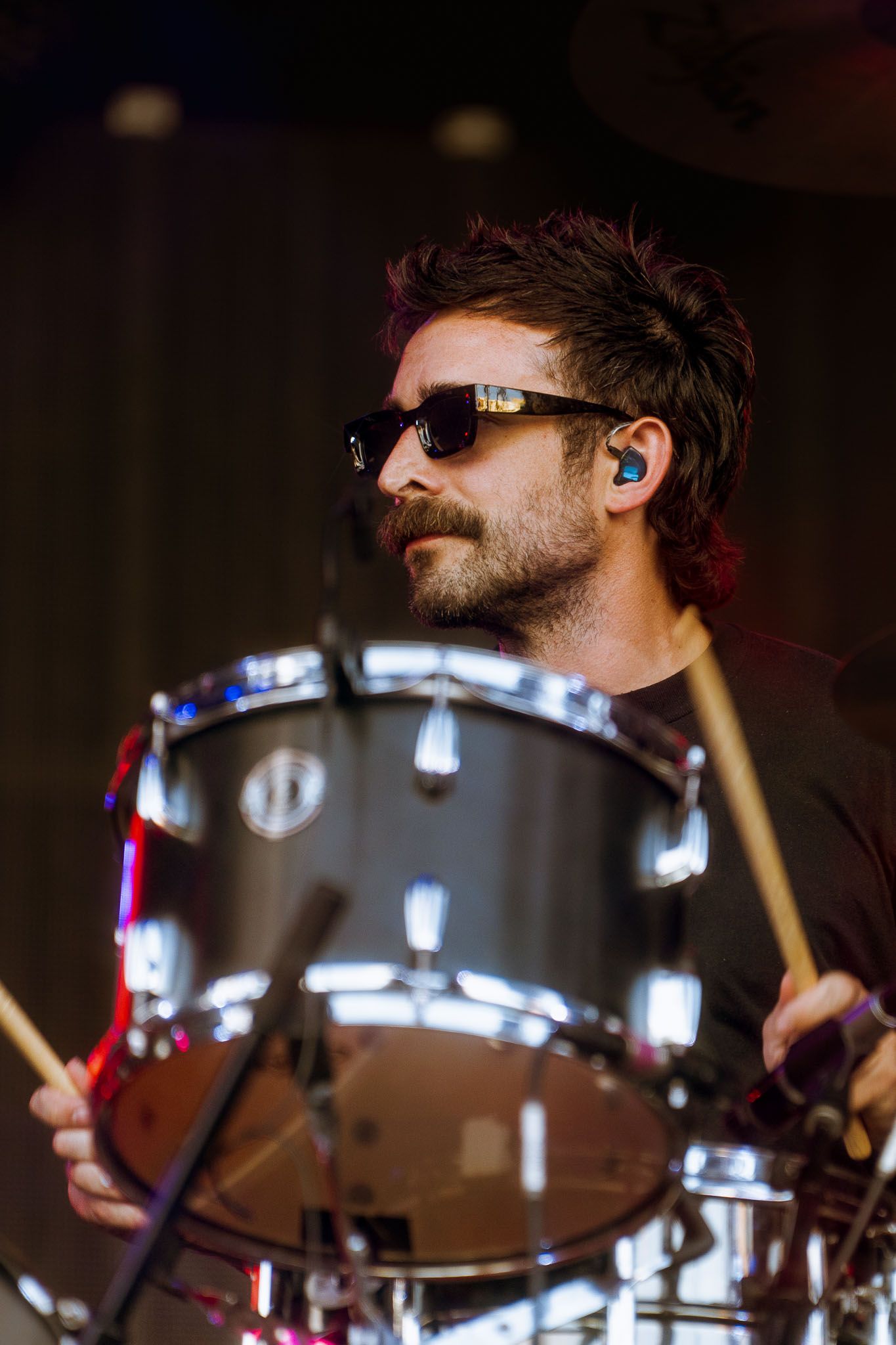 Close-up shot of drummer performing behind drum kit with stage lighting effects.