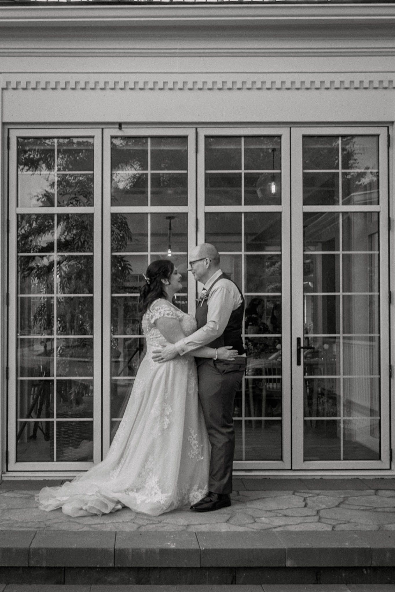 Black and white sequence of wedding couple dancing outside a building with large windows.