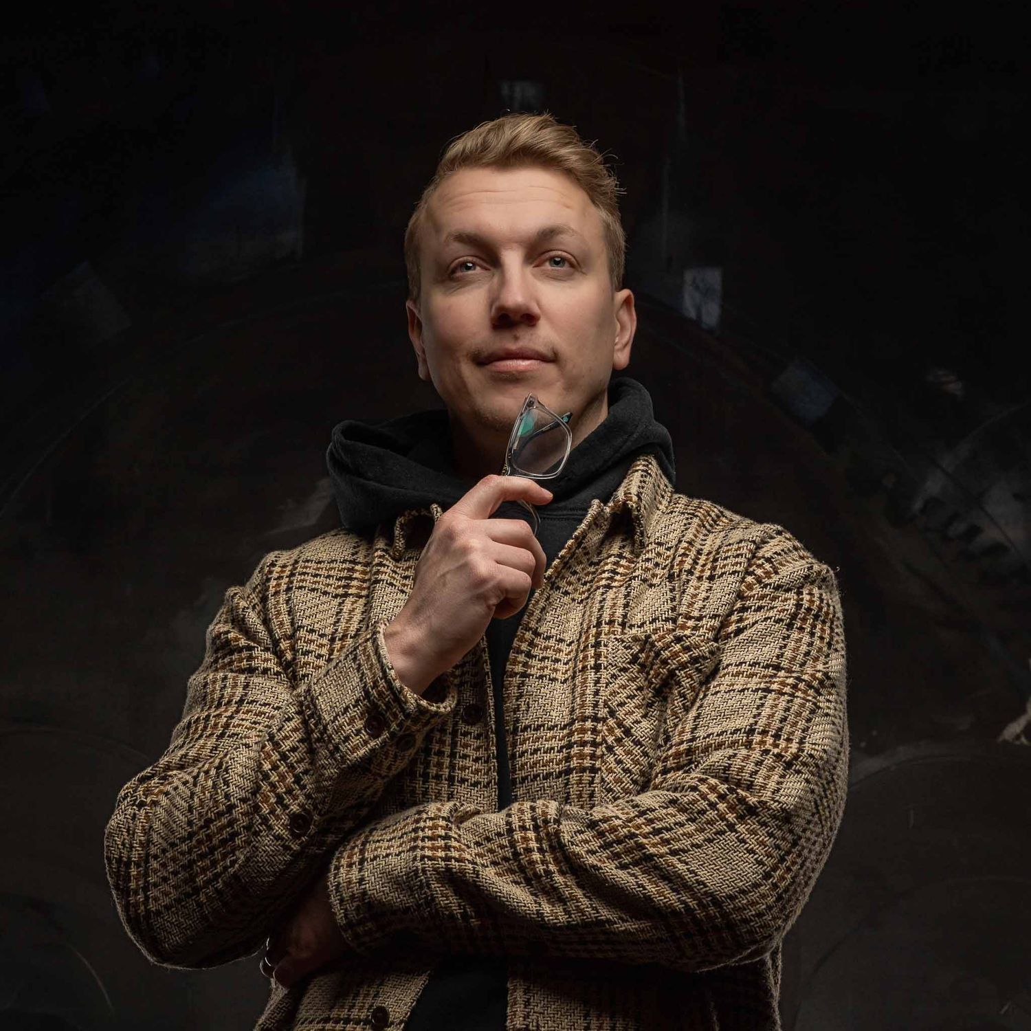 Portrait of person in plaid jacket with headphones against dark background.