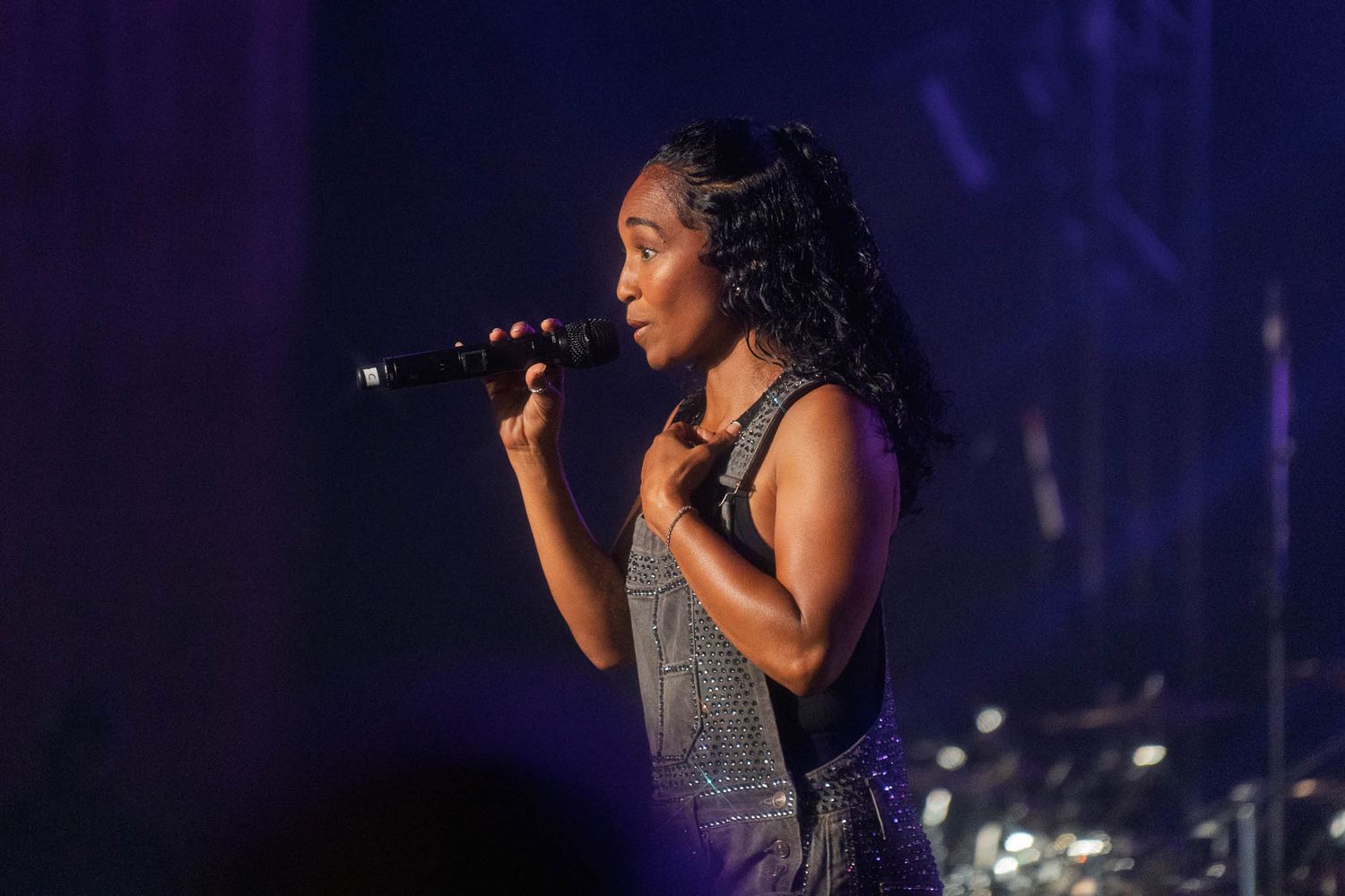 TLC performs with microphone on dimly lit stage during concert.