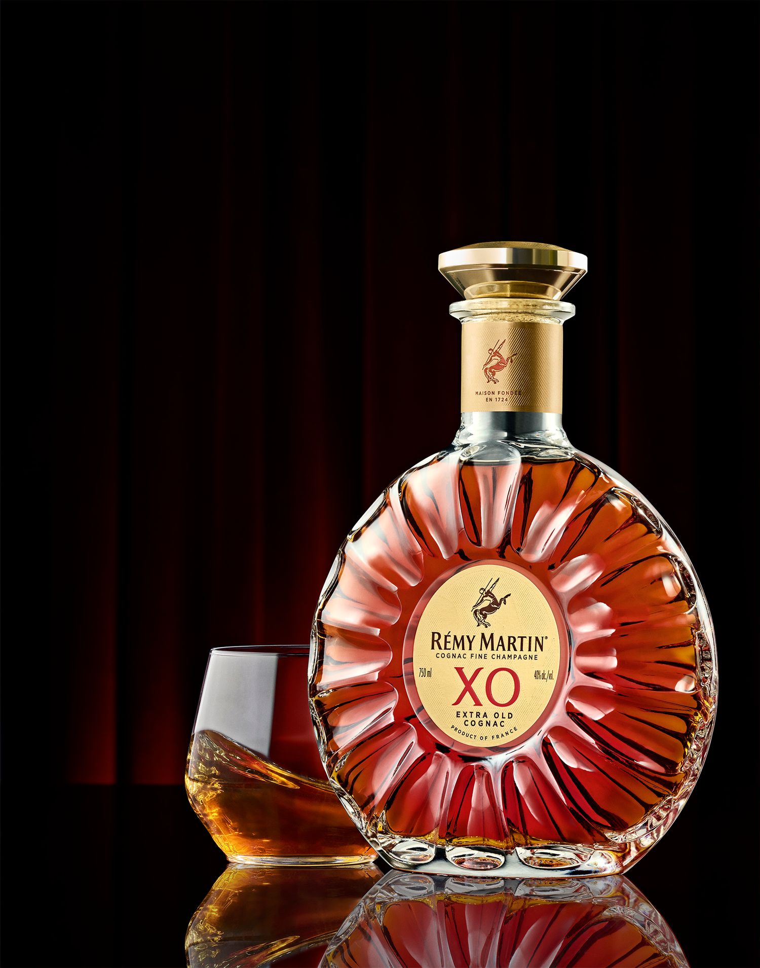 Rémy Martin XO Extra Old Cognac bottle with a glass, displayed against a dark red background.